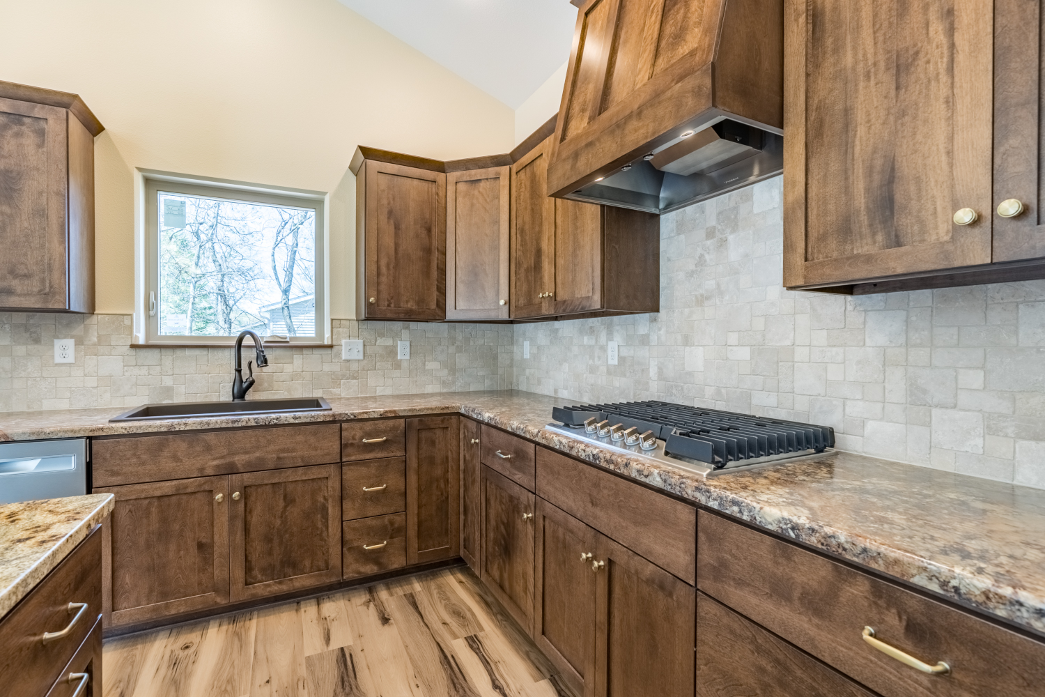 Kitchen with wooden cabinets, beige tile backsplash, granite countertops, and a window above the sink