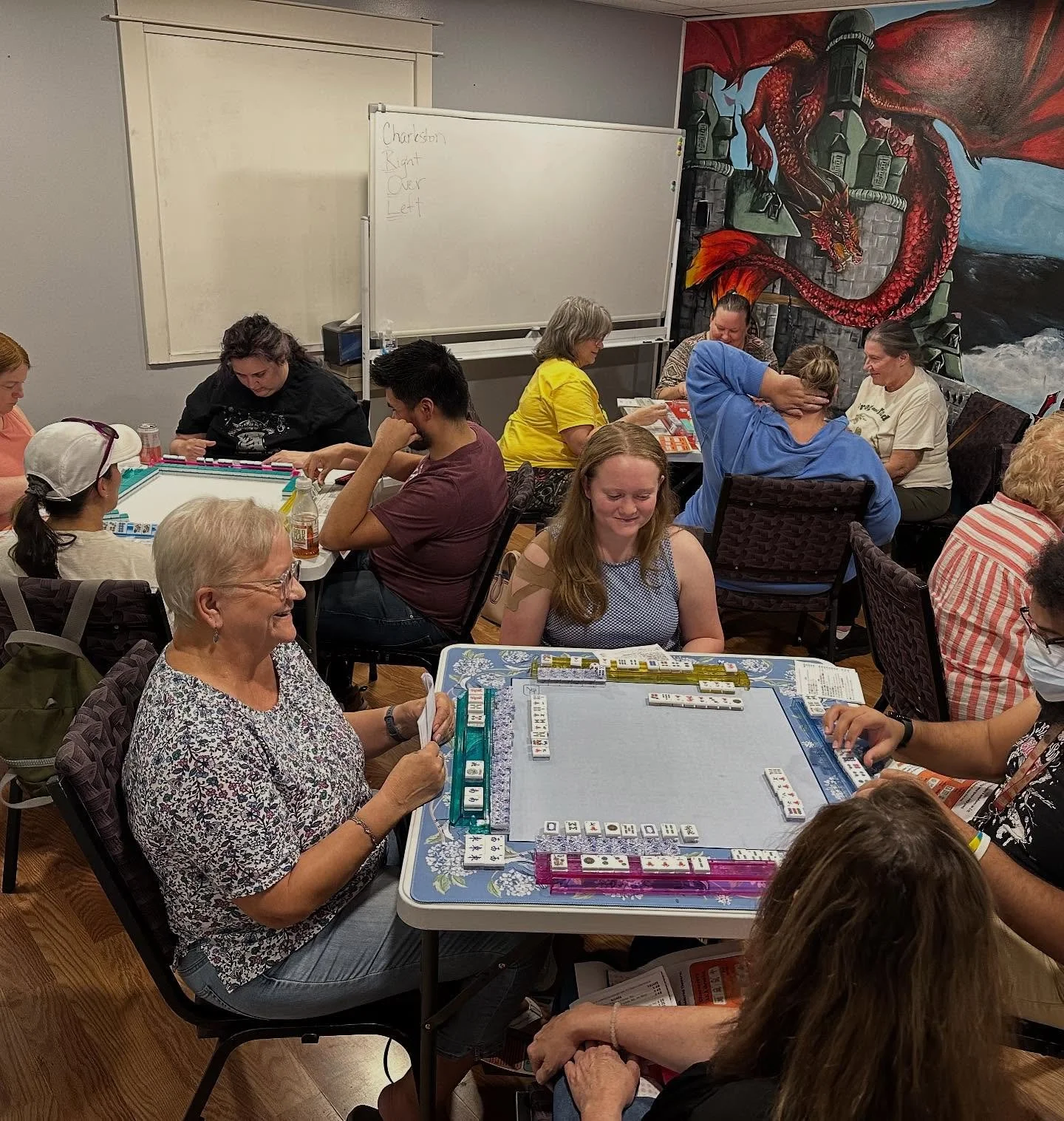 Group of five women standing together indoors, smiling, with some wearing matching 'Village Meeple Minion' T-shirts featuring a yellow minion figure.
