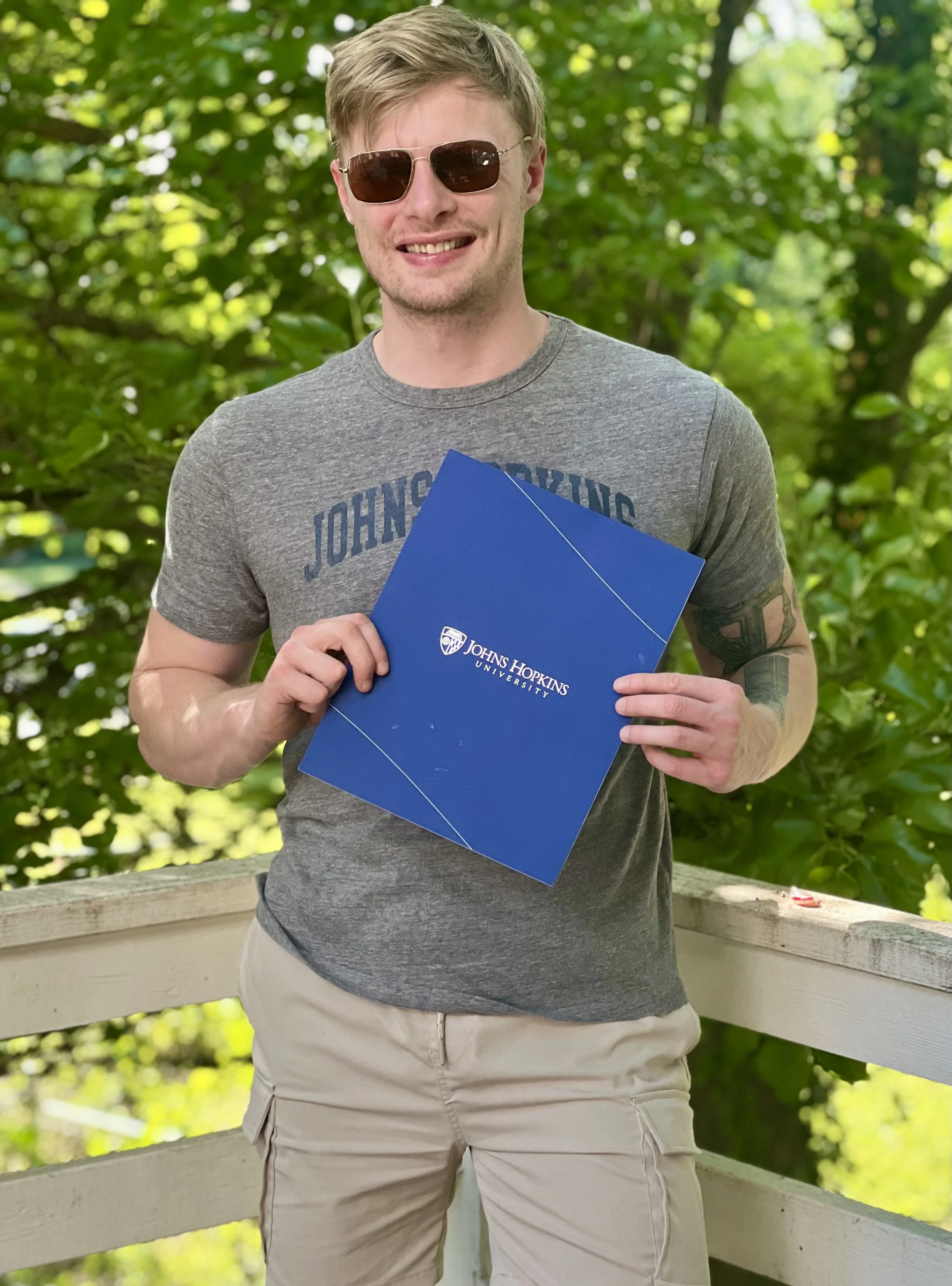 Person in sunglasses holding a Johns Hopkins University folder outdoors.