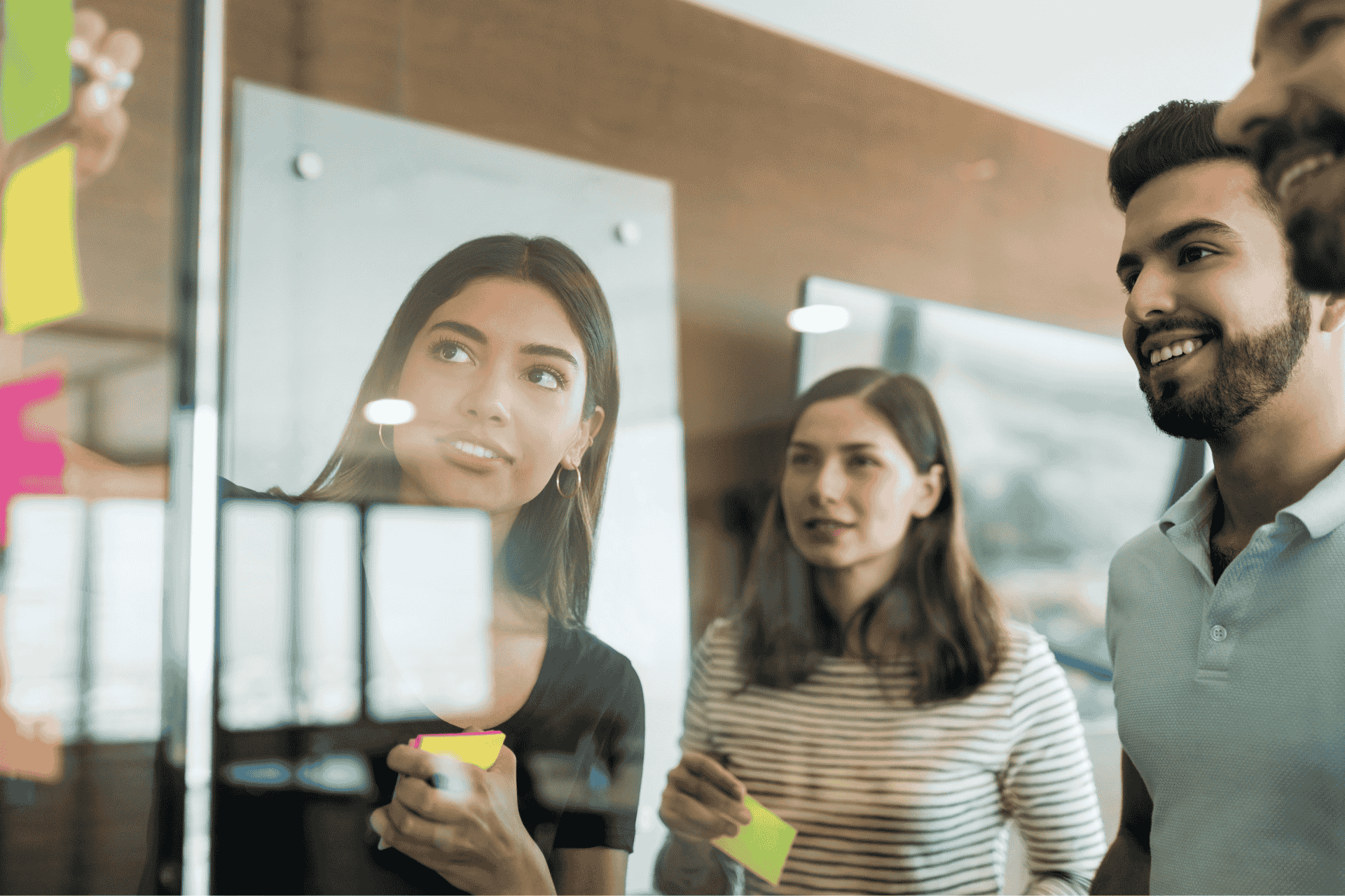 Two women and two men face a board and place sticky notes on to it during a strategic planning meeting.
