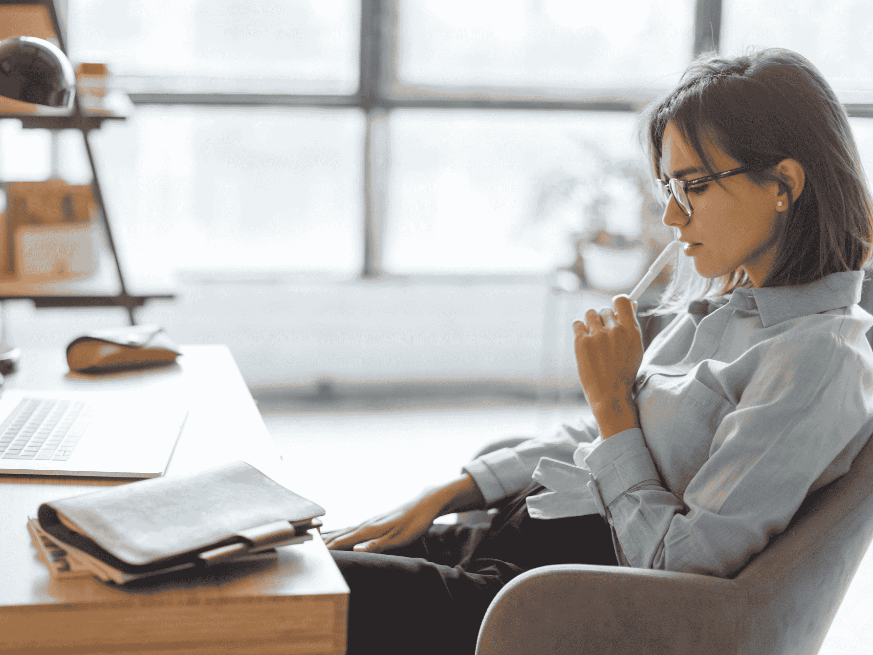 A woman sitting at desk thinking deeply with pen to chin showing she is concentrating on new business ideas.