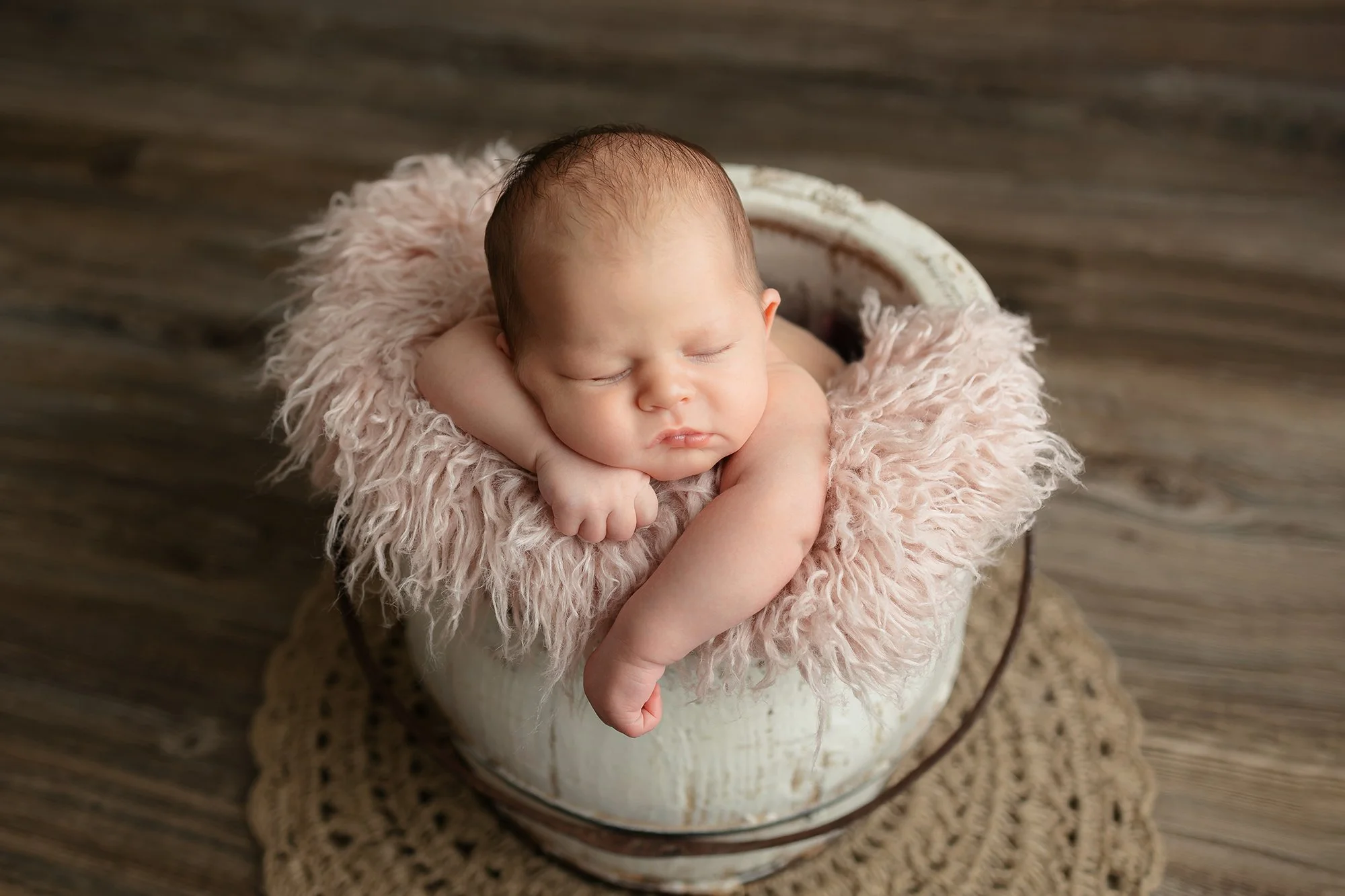 Sleep baby girl posing safely in a rustic wooden bucket.