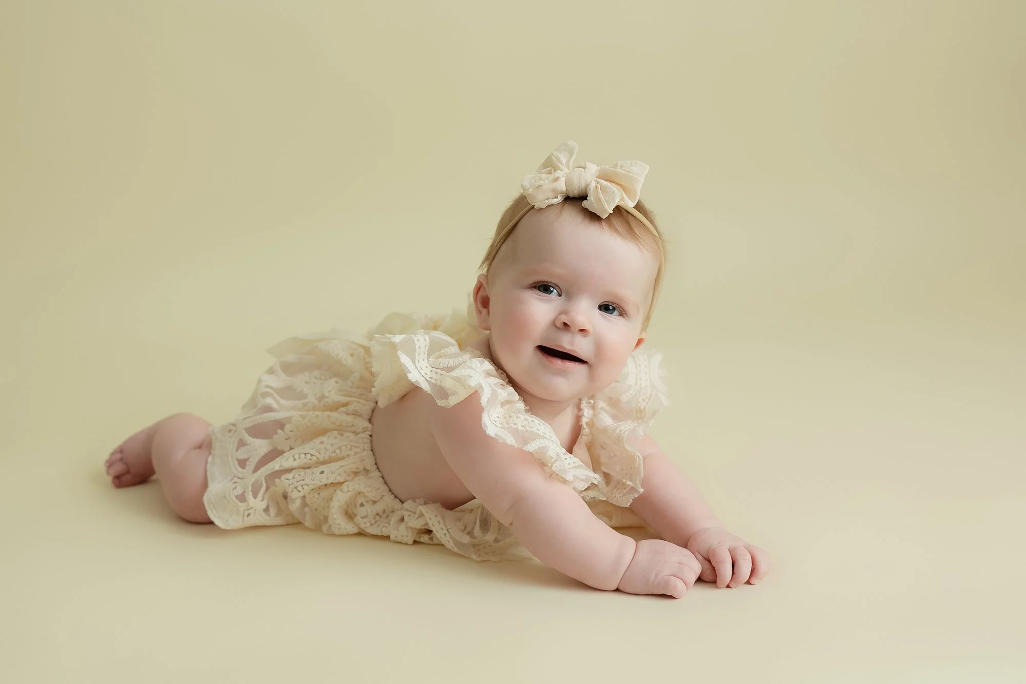 Four-month-old baby girl pushing up on her arms with a joyful expression during a milestone photography session.