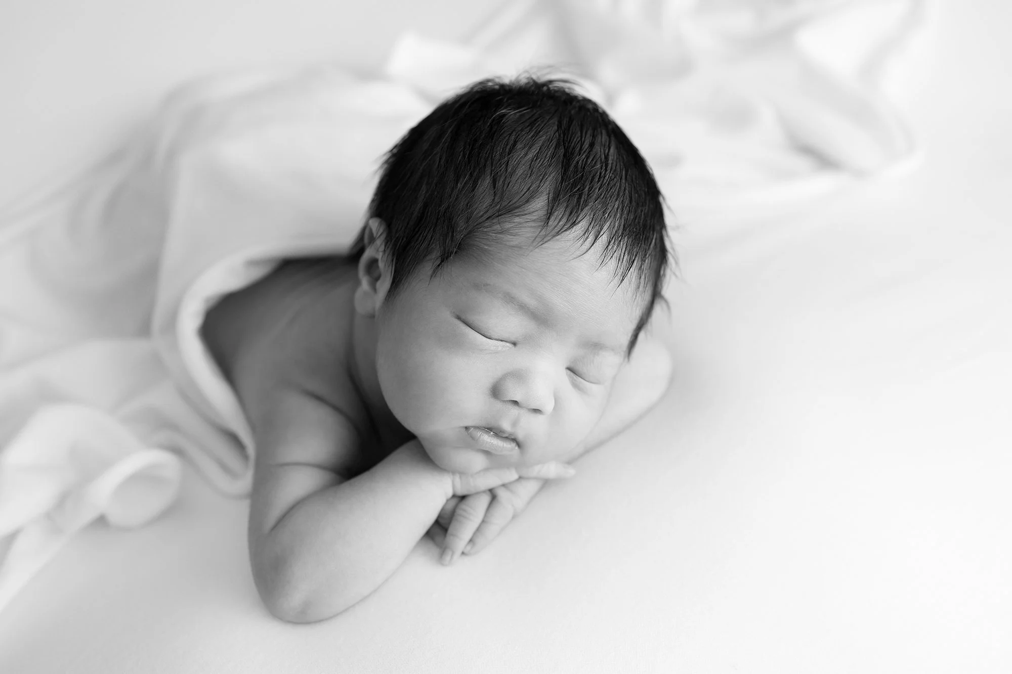 Artistic newborn session in Virginia: A sleepy baby boy posed with his hands under his chin.