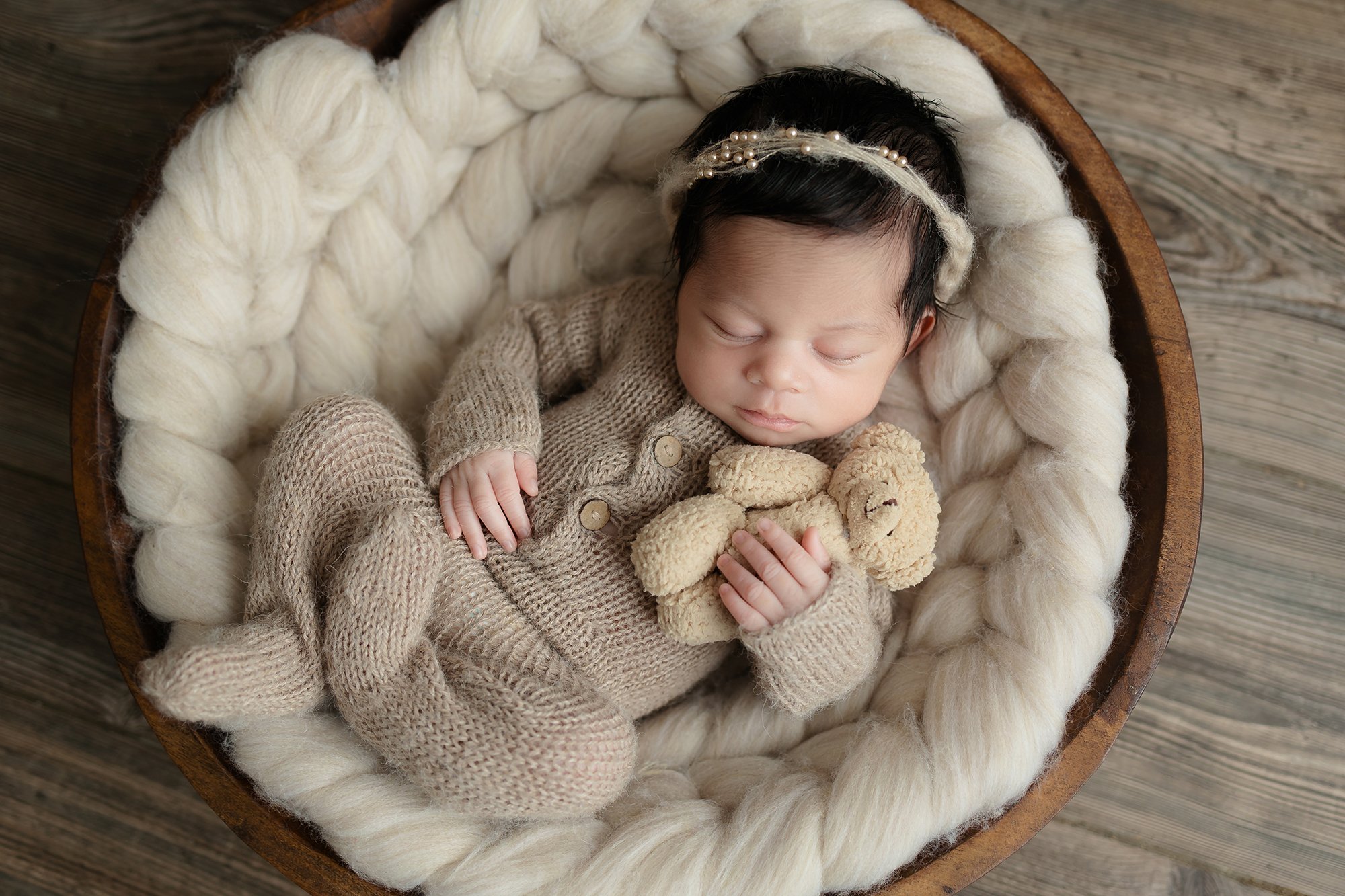 Newborn posing in a rustic bowl holding a little teddy bear prop.