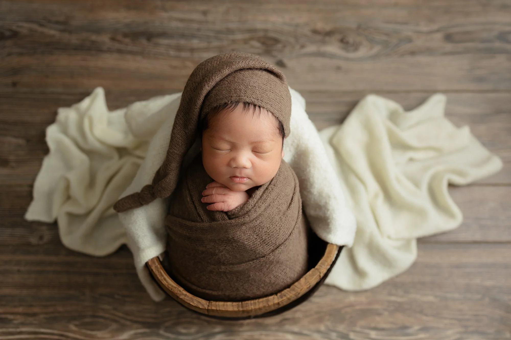 A simple newborn pose inside a shallow wooden bucket lined with artisan-crafted wool, emphasizing quality over quantity.