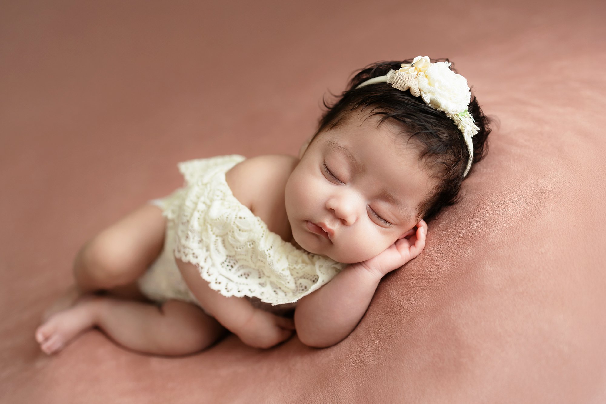 Expertly posed newborn baby girl with tiny hands tucked under her chin, showcasing delicate features and soft textures.