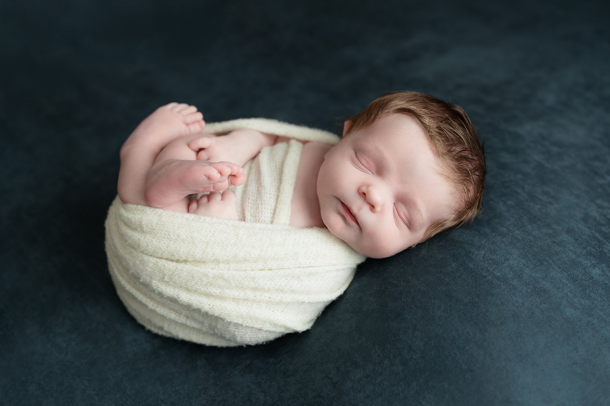 Baby boy safely posing on his side in a soft wool wrap.