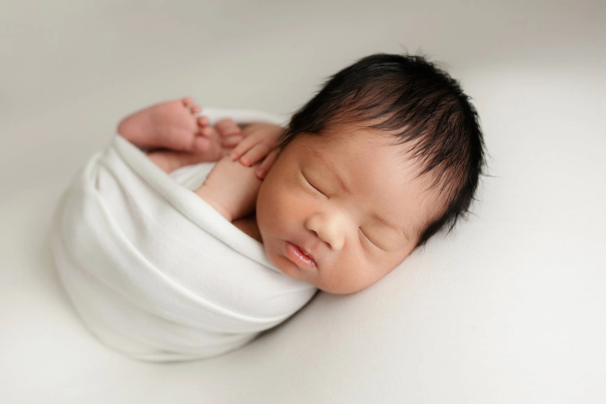Simplistic newborn baby posing in a white wrap.