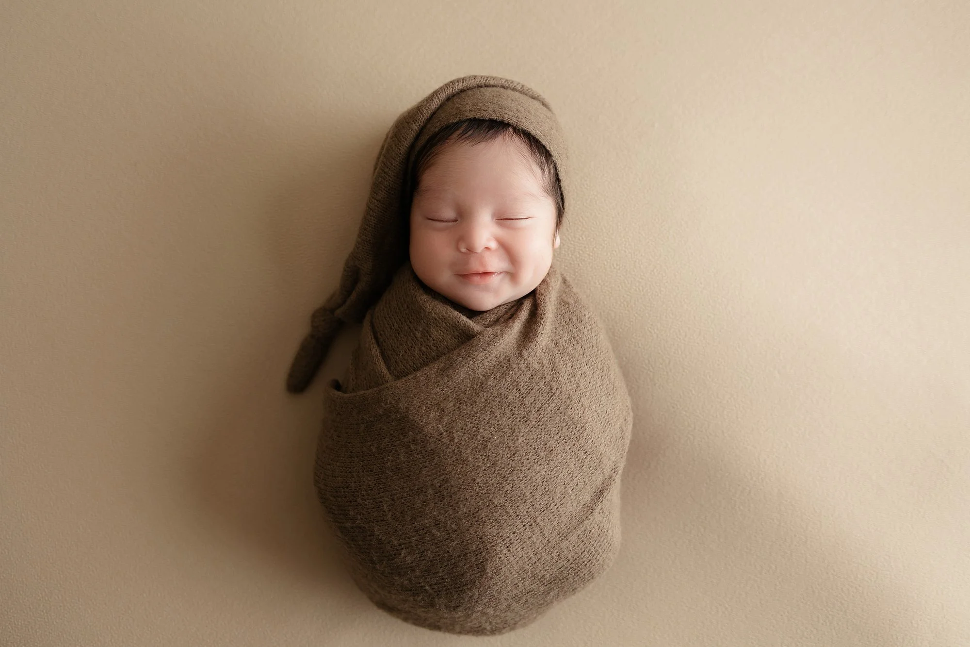 Posed newborn baby boy sleeping in a brown knit wrap by a professional photographer in Manassas, Virginia
