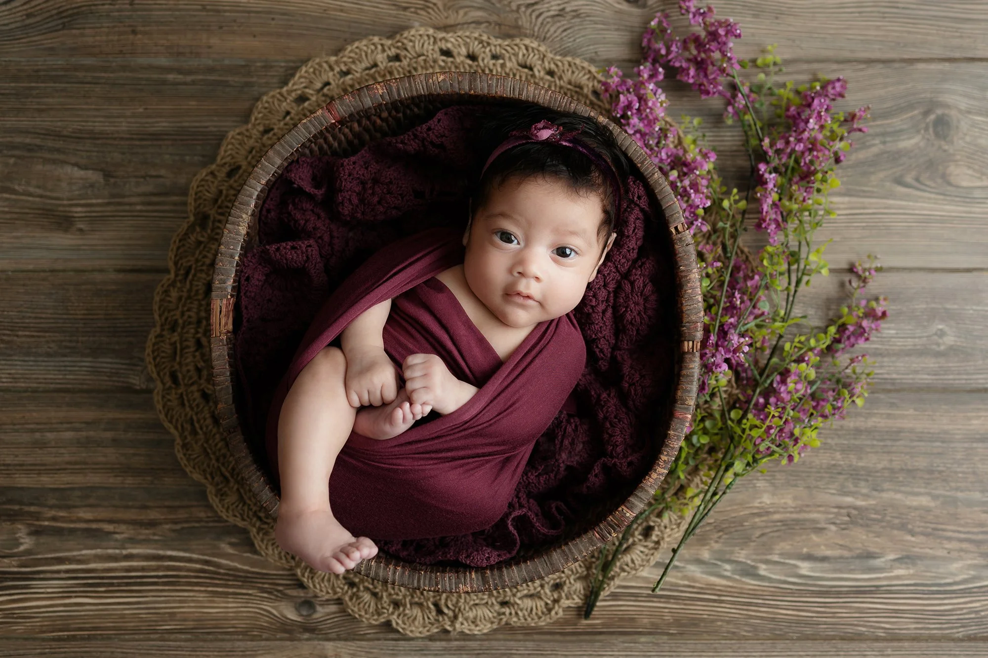 Newborn baby safely posed in a simple wooden bowl prop for a high-impact petite session.