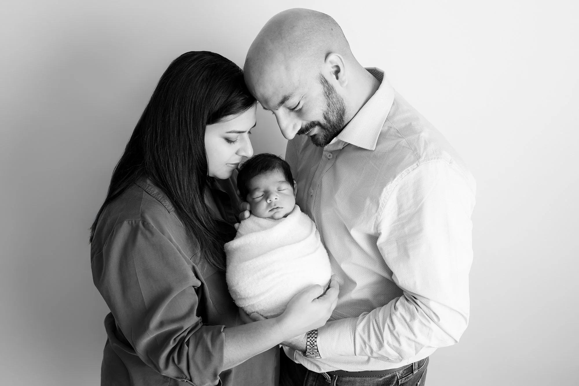 Black and white portrait of a mother and father holding their newborn baby close, celebrating the raw, authentic bond of parenthood.