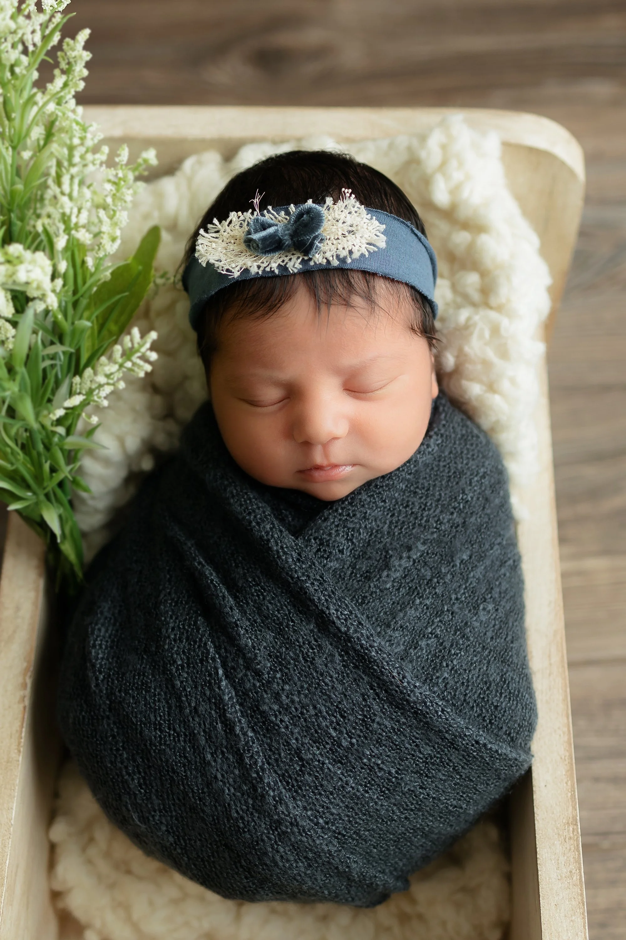 Baby girl posing in a cream bed with pretty flowers surrounding her.