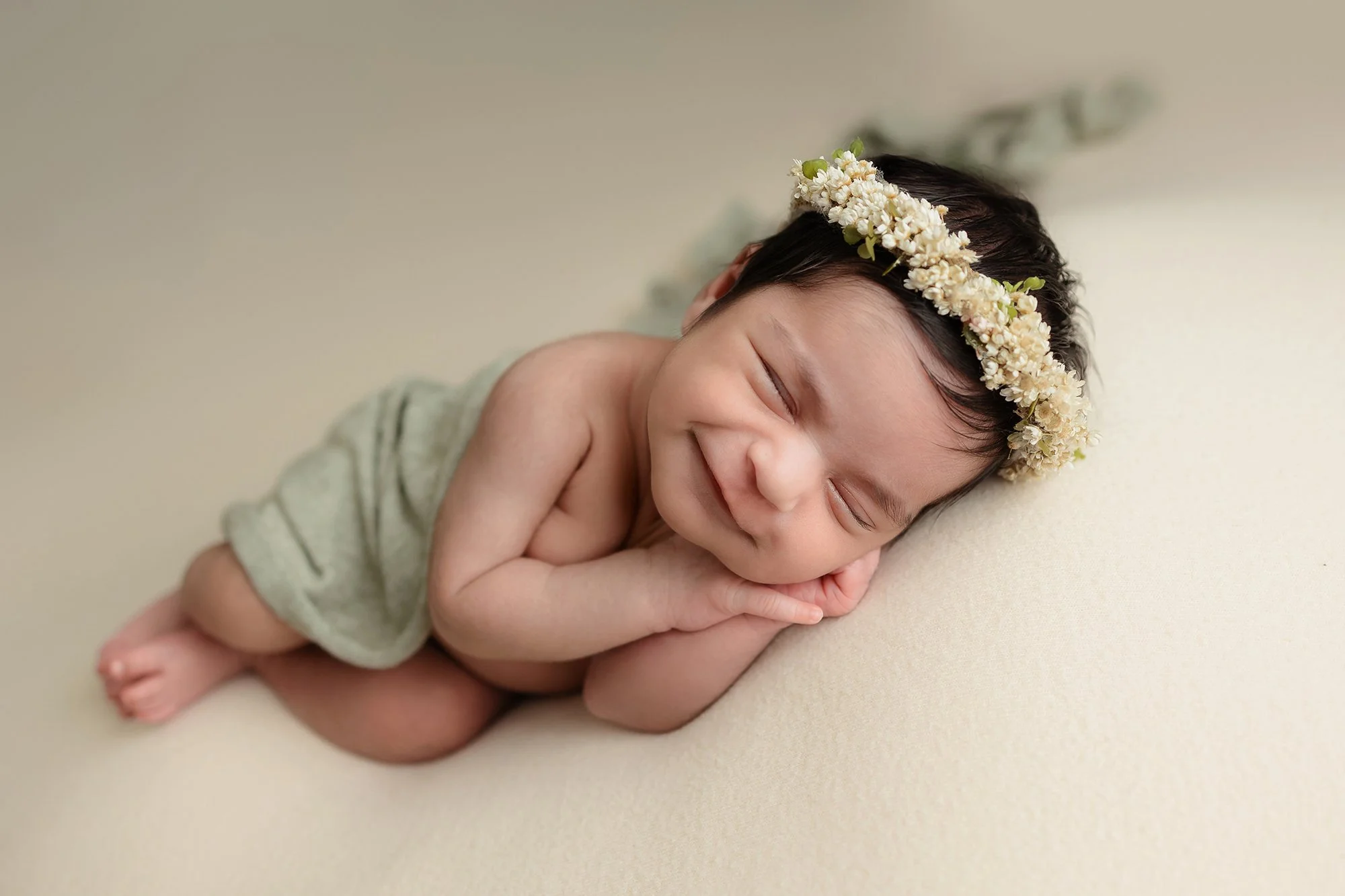 A sweet newborn baby girl wearing a delicate floral headband, sleeping peacefully and flashing a tiny smile while wrapped in a soft pink swaddle in Manassas, VA