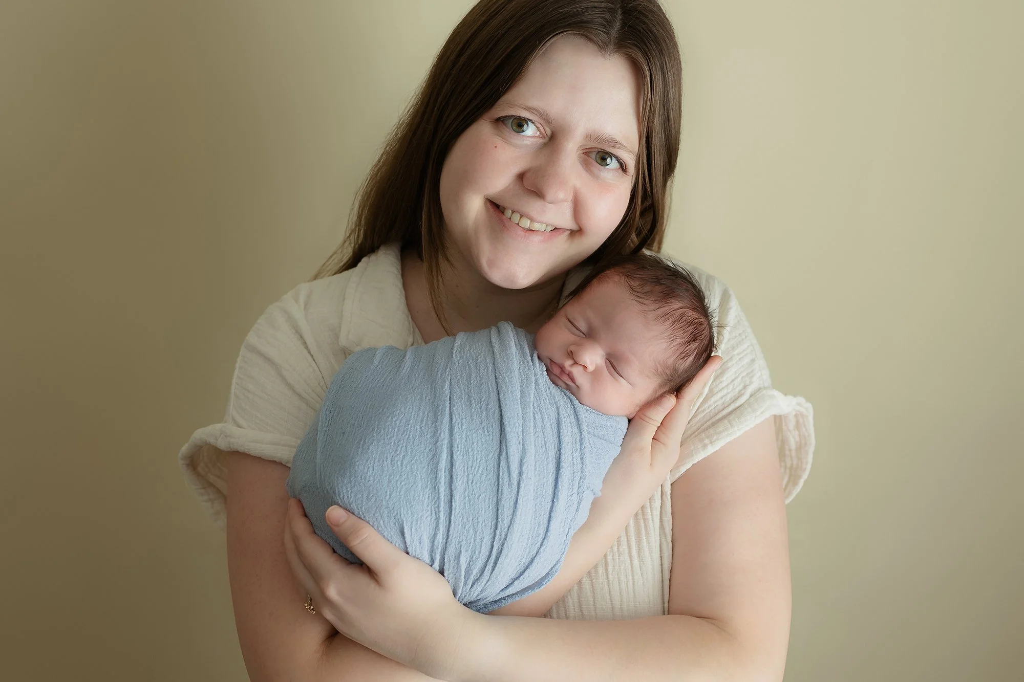 New mother posing with her sweet swaddled newborn boy for her first portrait session.