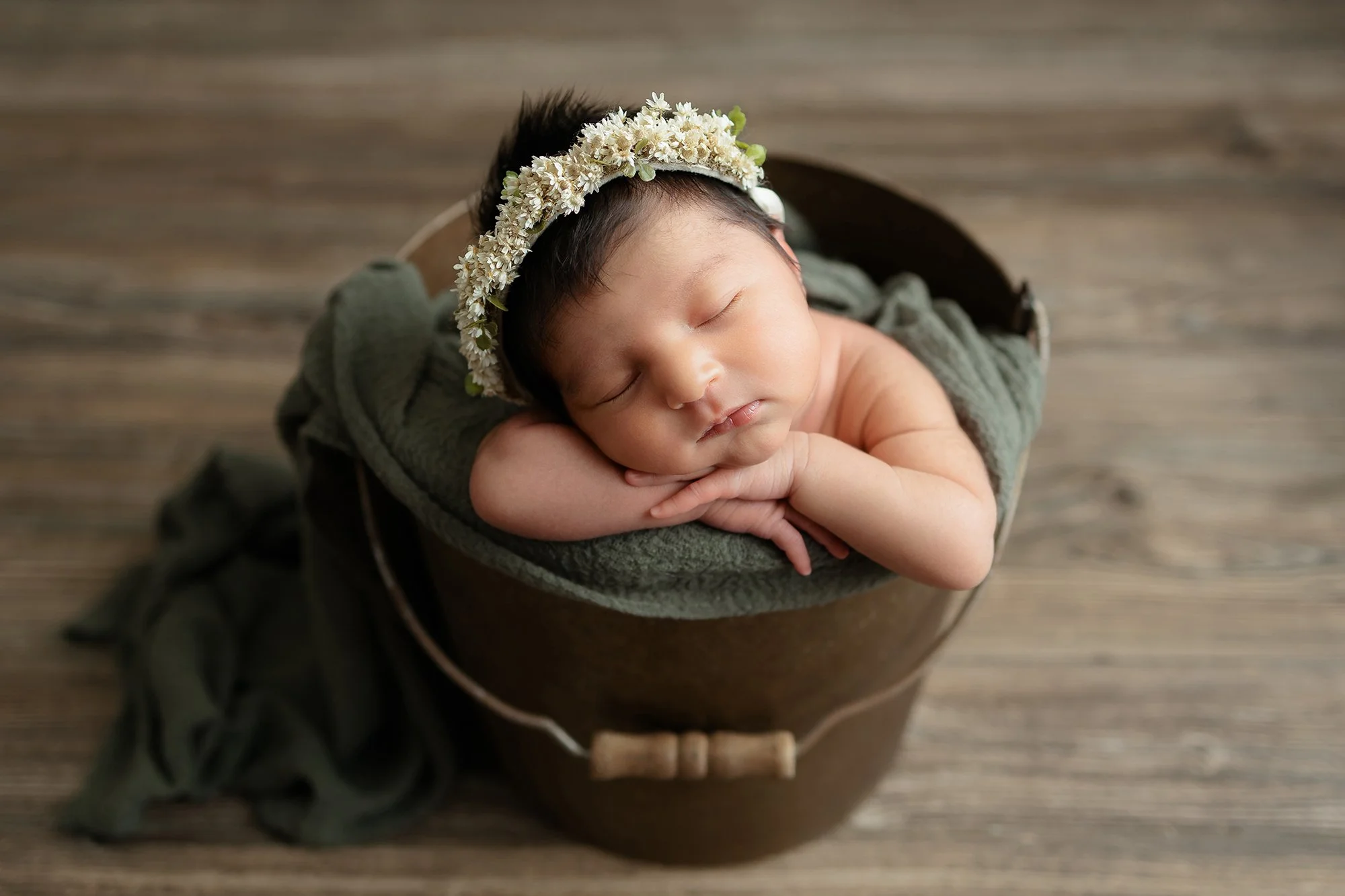 Posed newborn baby girl sleeping in a vintage wooden bucket by a professional newborn photographer in Woodbridge, Virginia
