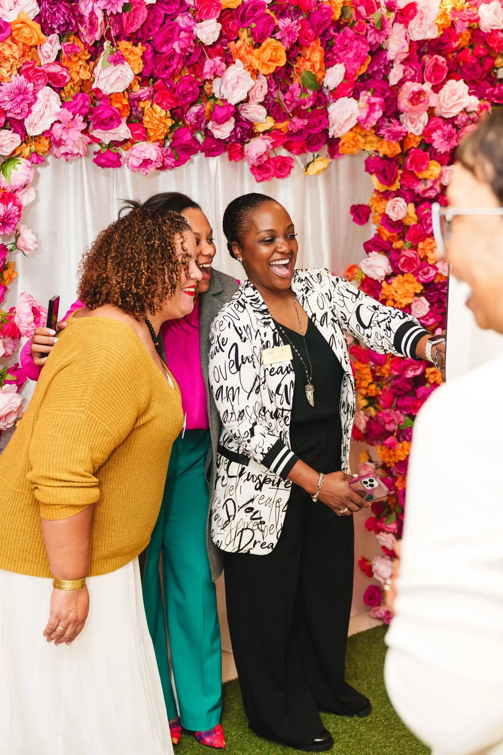Group of women smiling and taking a selfie in front of a colorful floral backdrop.