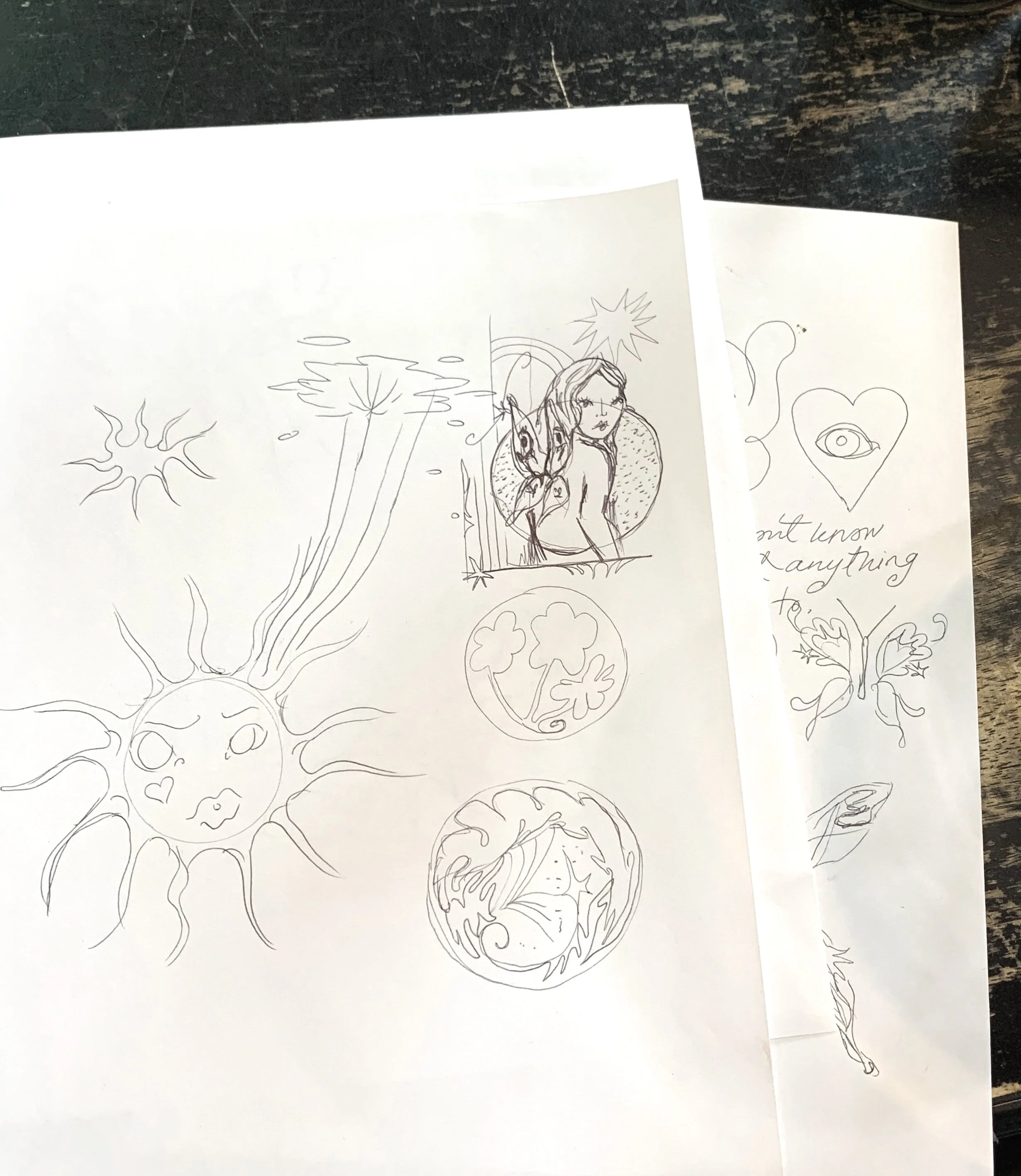 Sketches including a smiling sun with rays, a woman with long hair, two clover symbols, a face with closed eyes, a butterfly with a heart-shaped body, and some handwritten words.