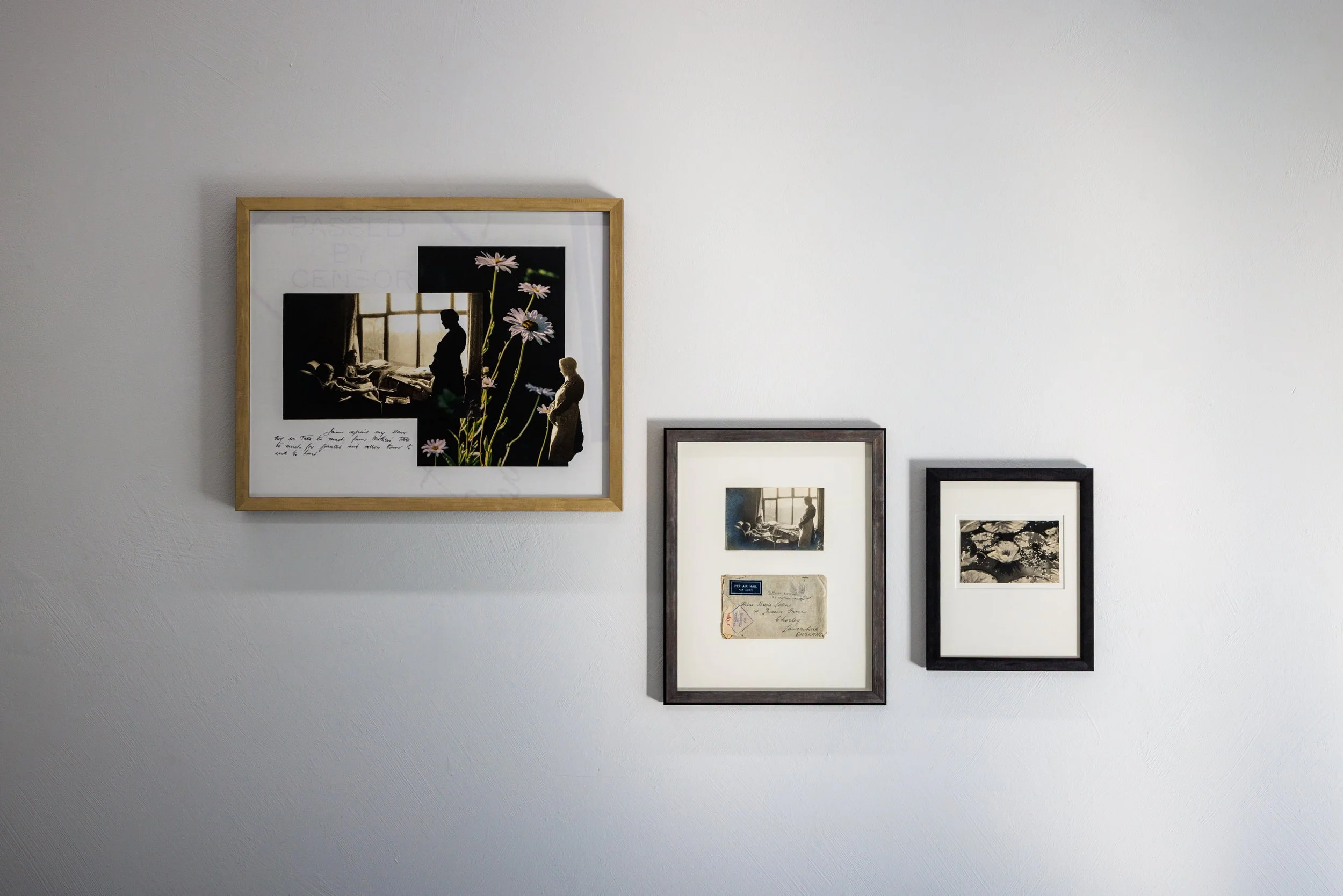 A white wall decorated with three photo frames, including a larger one with a collage of black-and-white photos and artistic overlays of yellow daisies.