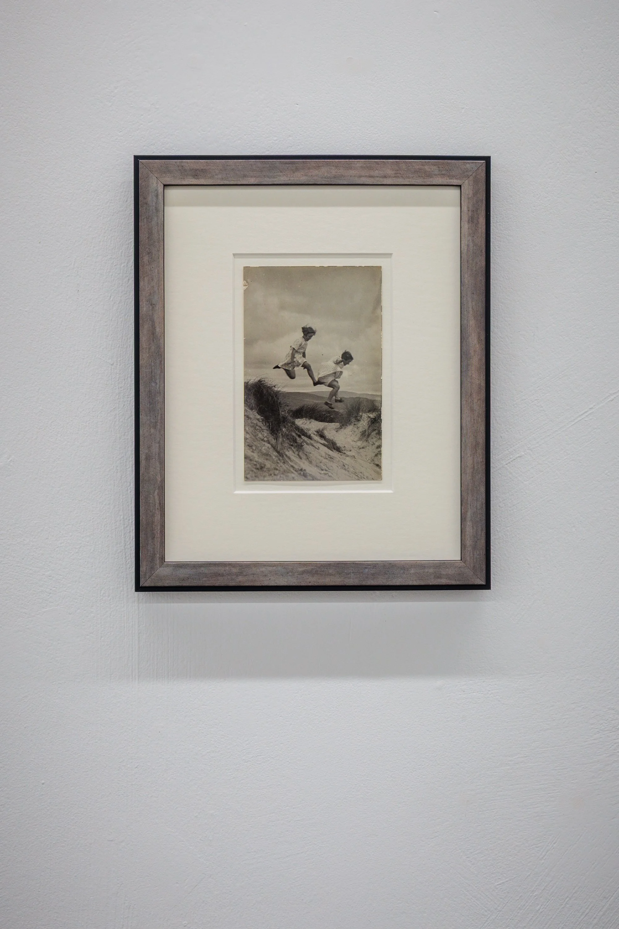 Black and white photograph of two children jumping on a sandy landscape with hills in the background and a cloudy sky.