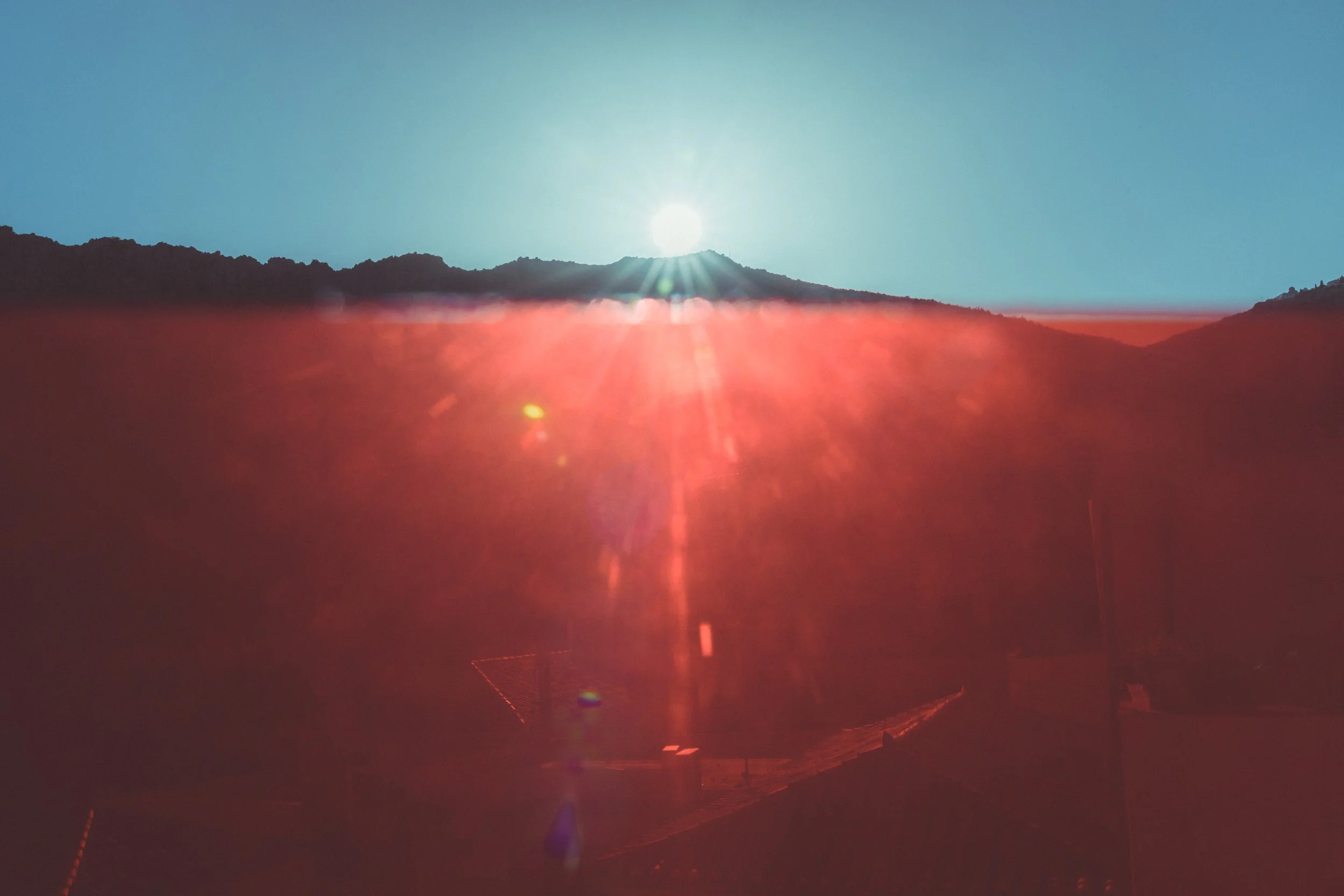 Sunrise over mountains with lens flare and a red gel in the foreground.