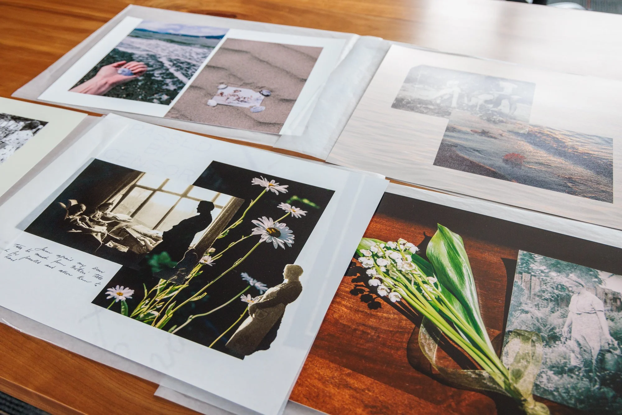 Printed photographs of beach scenes, flowers, and people, spread across papers on a wooden table.