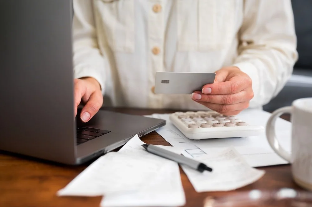 Person holding a credit card next to a laptop, calculator, and receipts while setting up a monthly subscription payment
