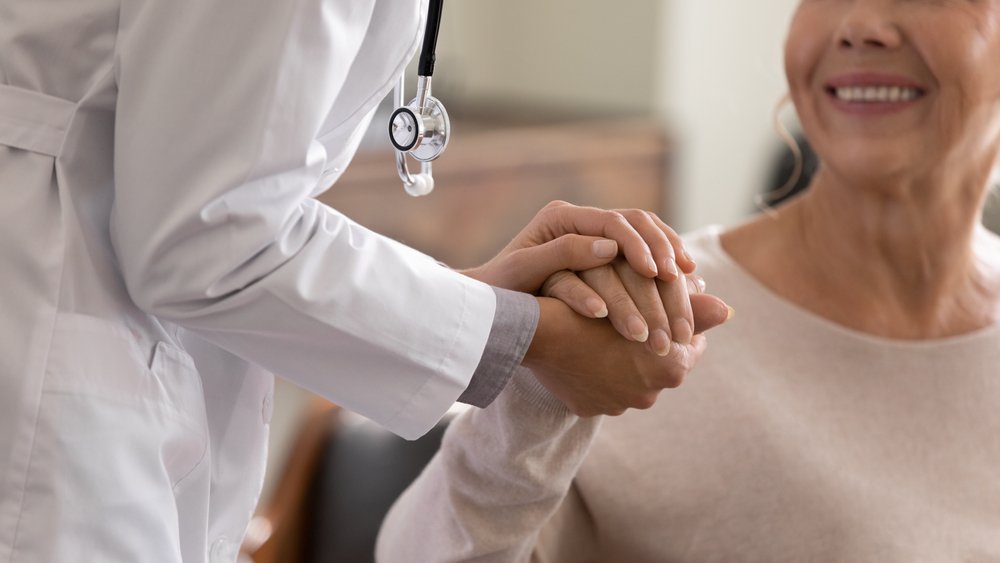 Closeup of a doctor's hand holding the hand of an older adult | Safer Sacramento