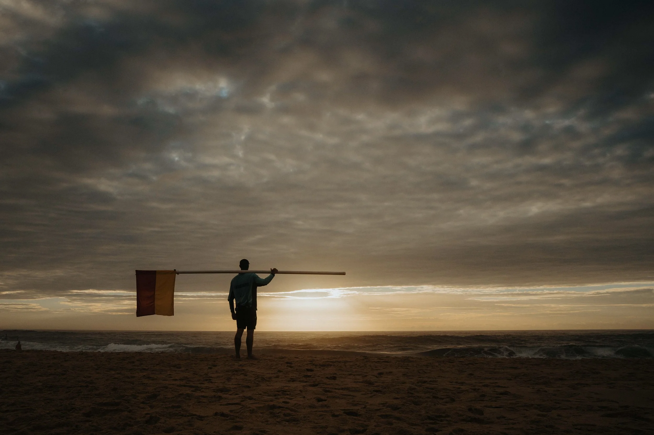 Surf lifeguard holding flag, sunrise