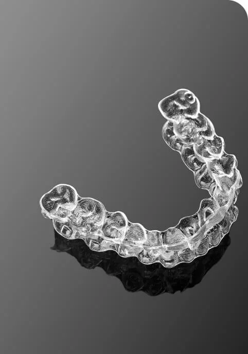 Clear dental aligner on a reflective black surface.