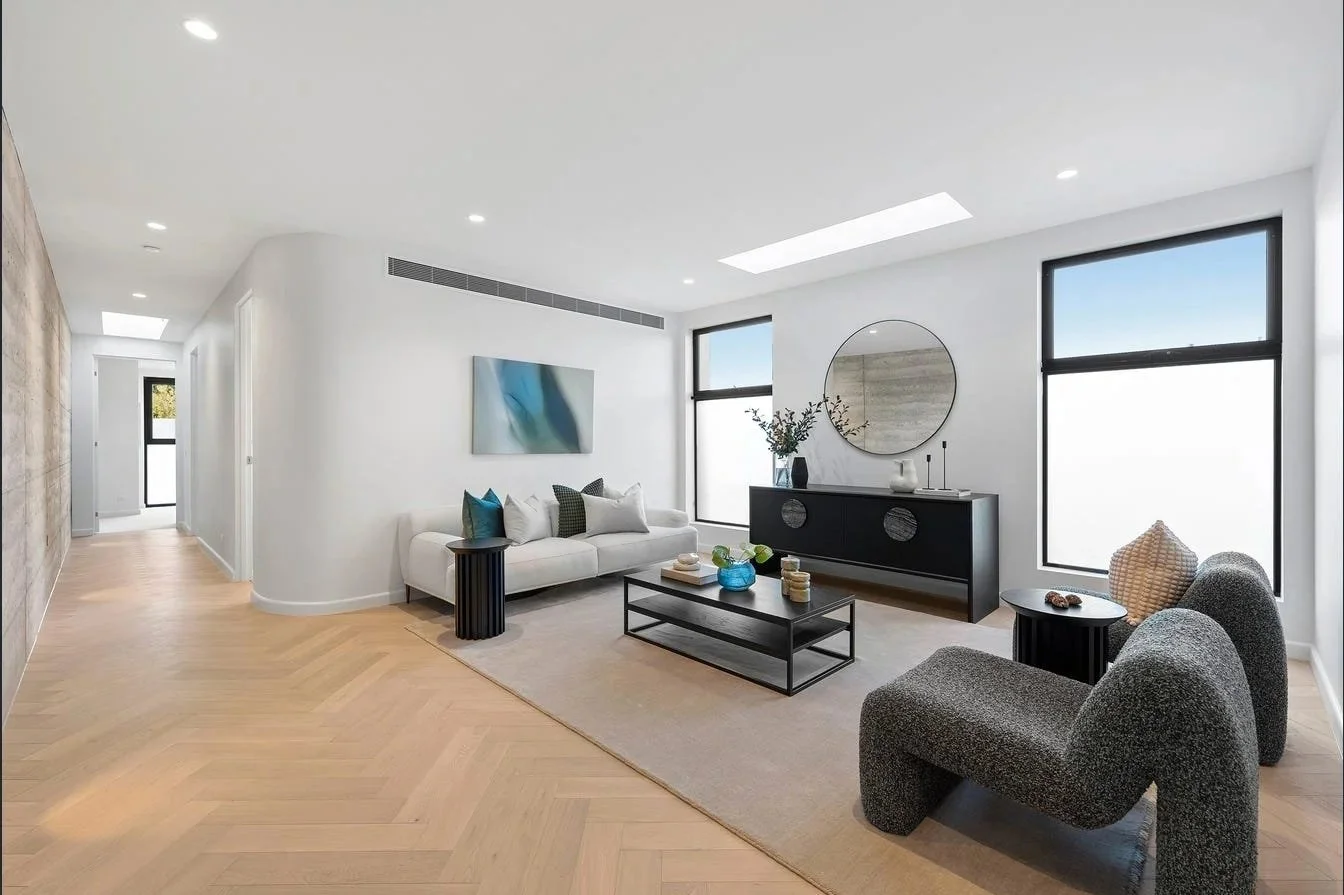Modern living room with white walls, hardwood floors, black and white furniture, large windows, wall art, and decorative items.