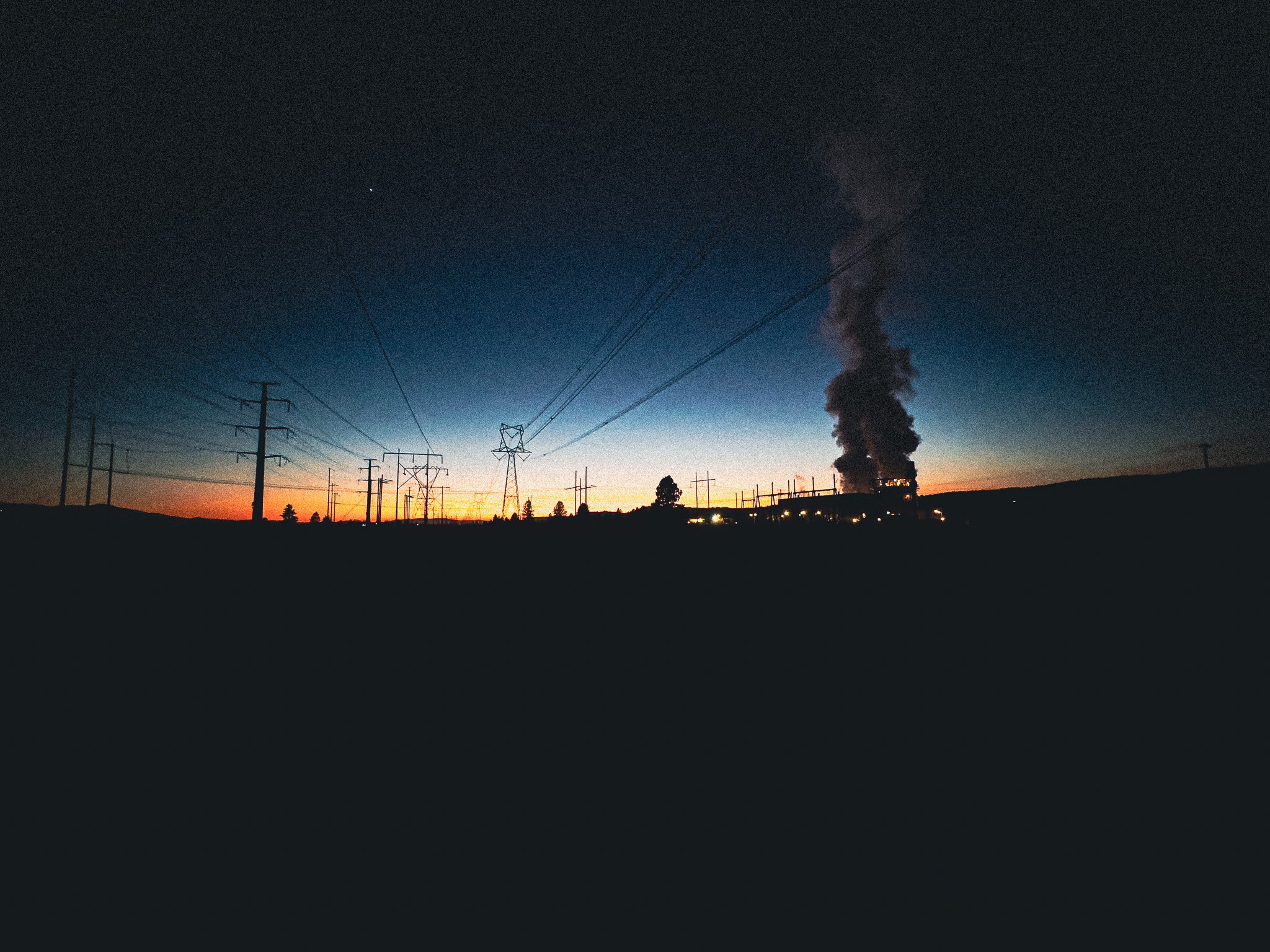 Silhouette of power lines and a smokestack at sunset
