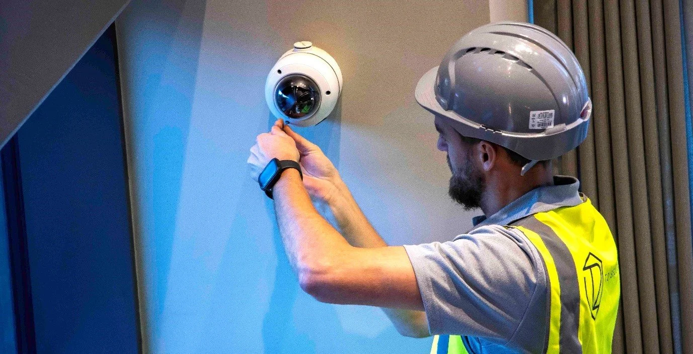Interior view of a modern shopping mall with multiple levels, escalators, and a glass ceiling letting in natural light.