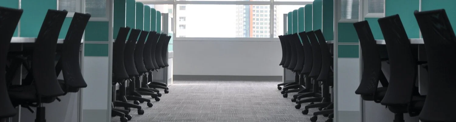 Empty office cubicles with black chairs in a modern office space.