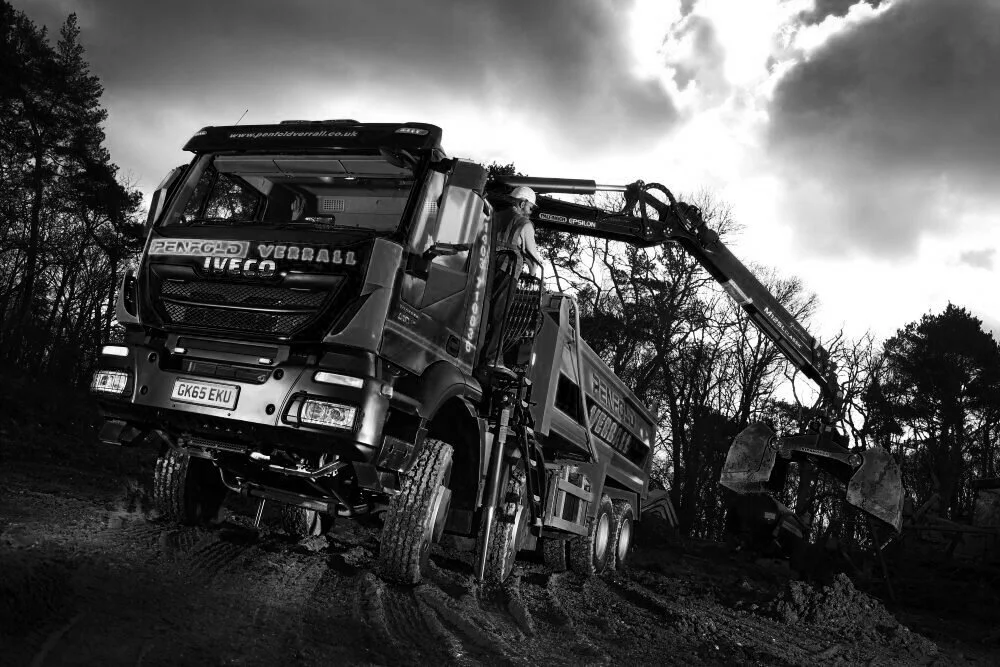 A large construction truck with a crane arm and digging bucket working outdoors during cloudy weather.