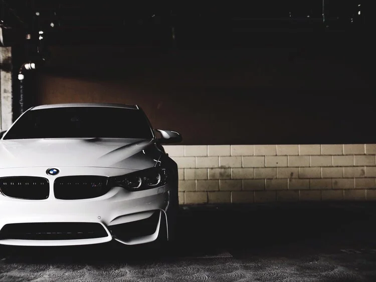 White BMW car parked in a dimly lit garage with a brick wall background.