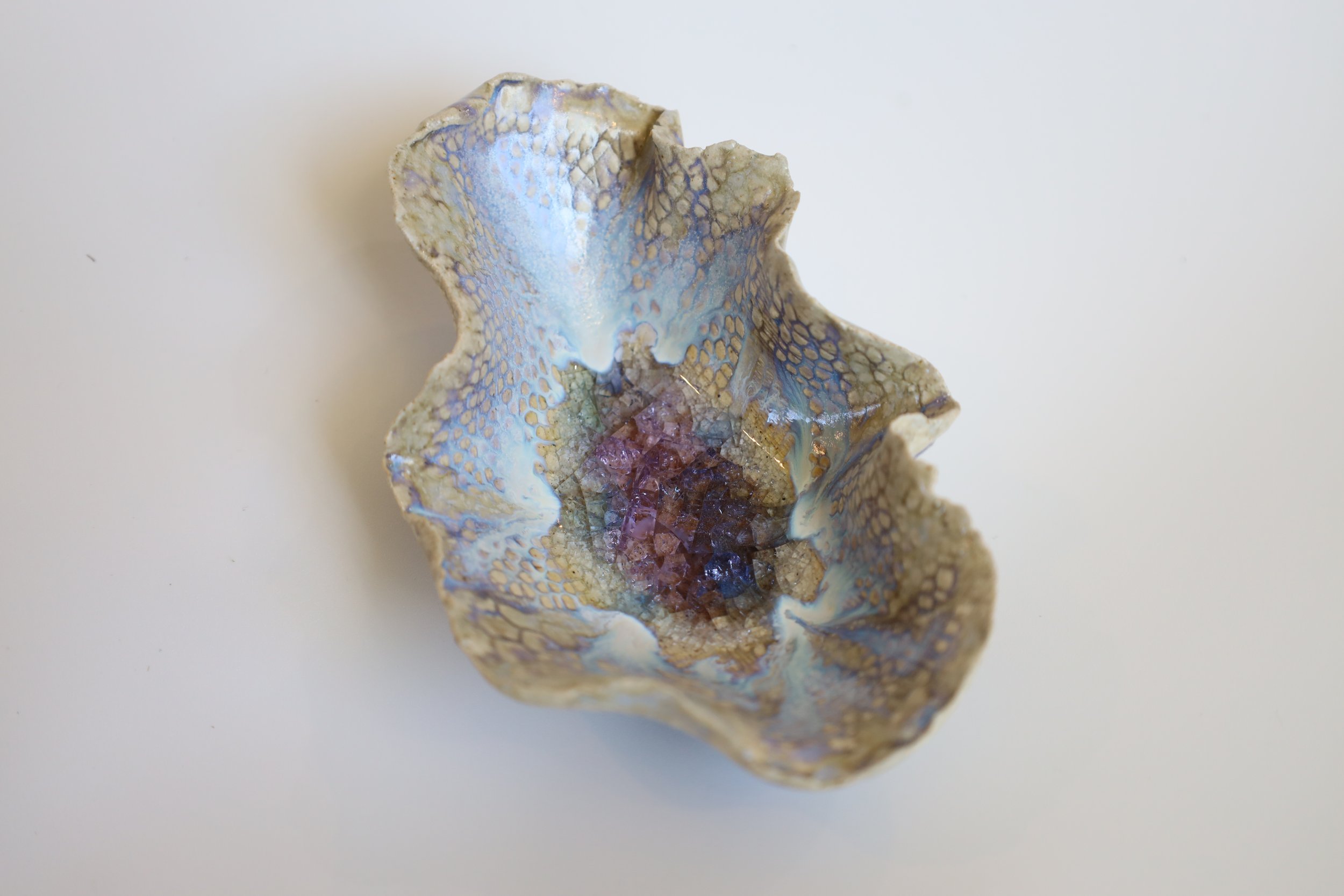 Decorative ceramic or glass sculpture with an irregular shape, featuring a textured surface with blue, purple, and cream-colored patterns.