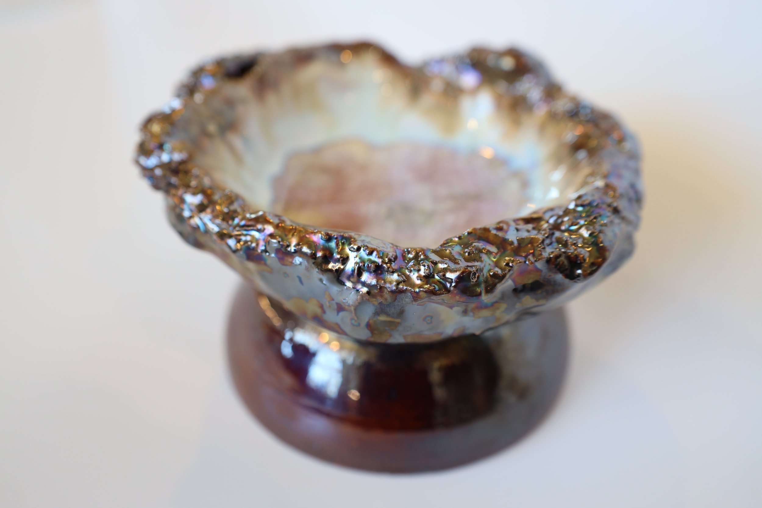 Close-up of a decorative iridescent bowl with a textured rim, sitting on a wooden base.
