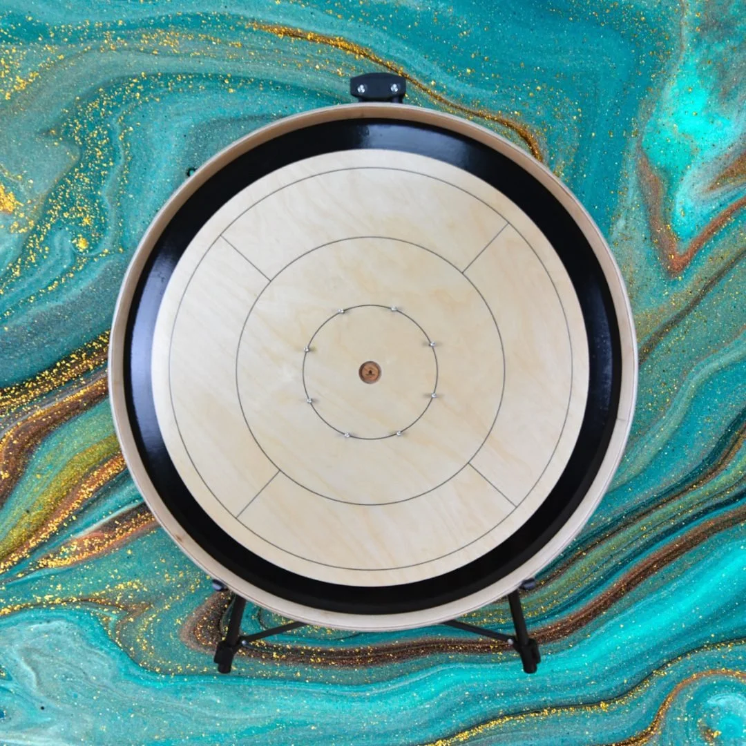 Natural wood Crokinole board with a black gutter on a turquoise and gold background