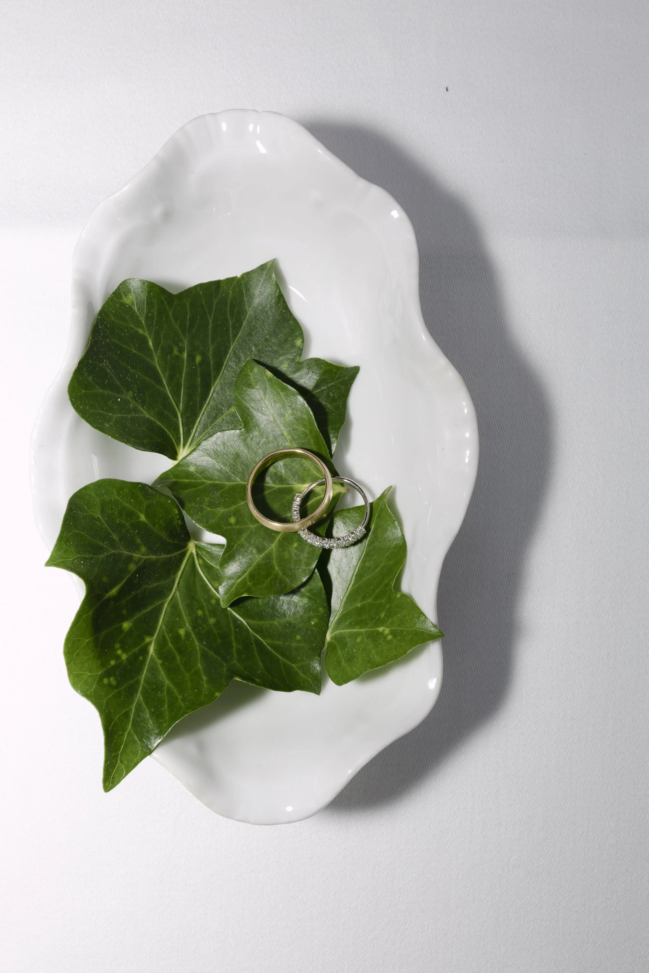 Deux alliances posées sur des feuilles de houx dans un plat blanc.