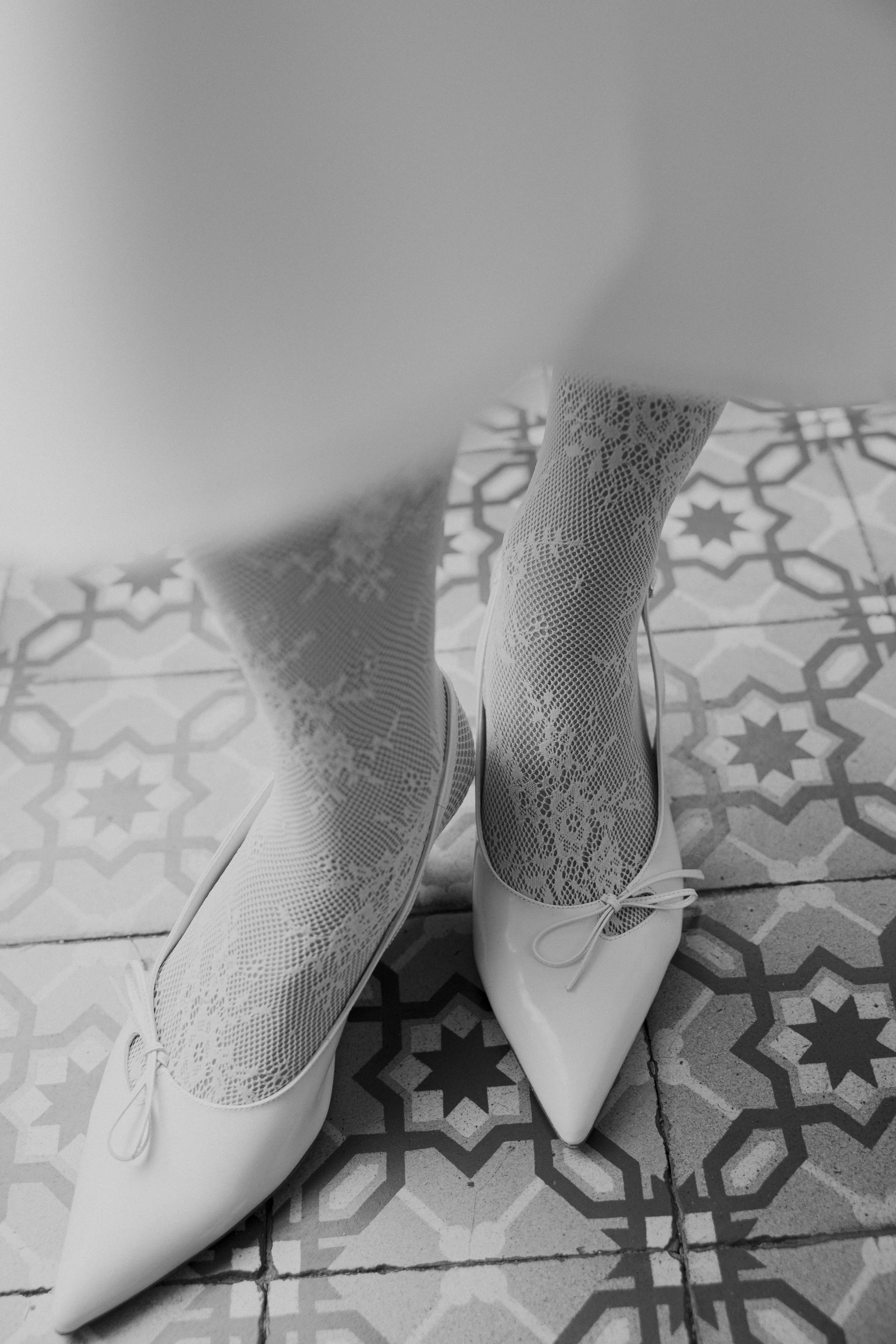 Chaussures blanches à talons avec des bas en dentelle à motifs floraux et géométriques, sur un sol en carreaux décoratifs.