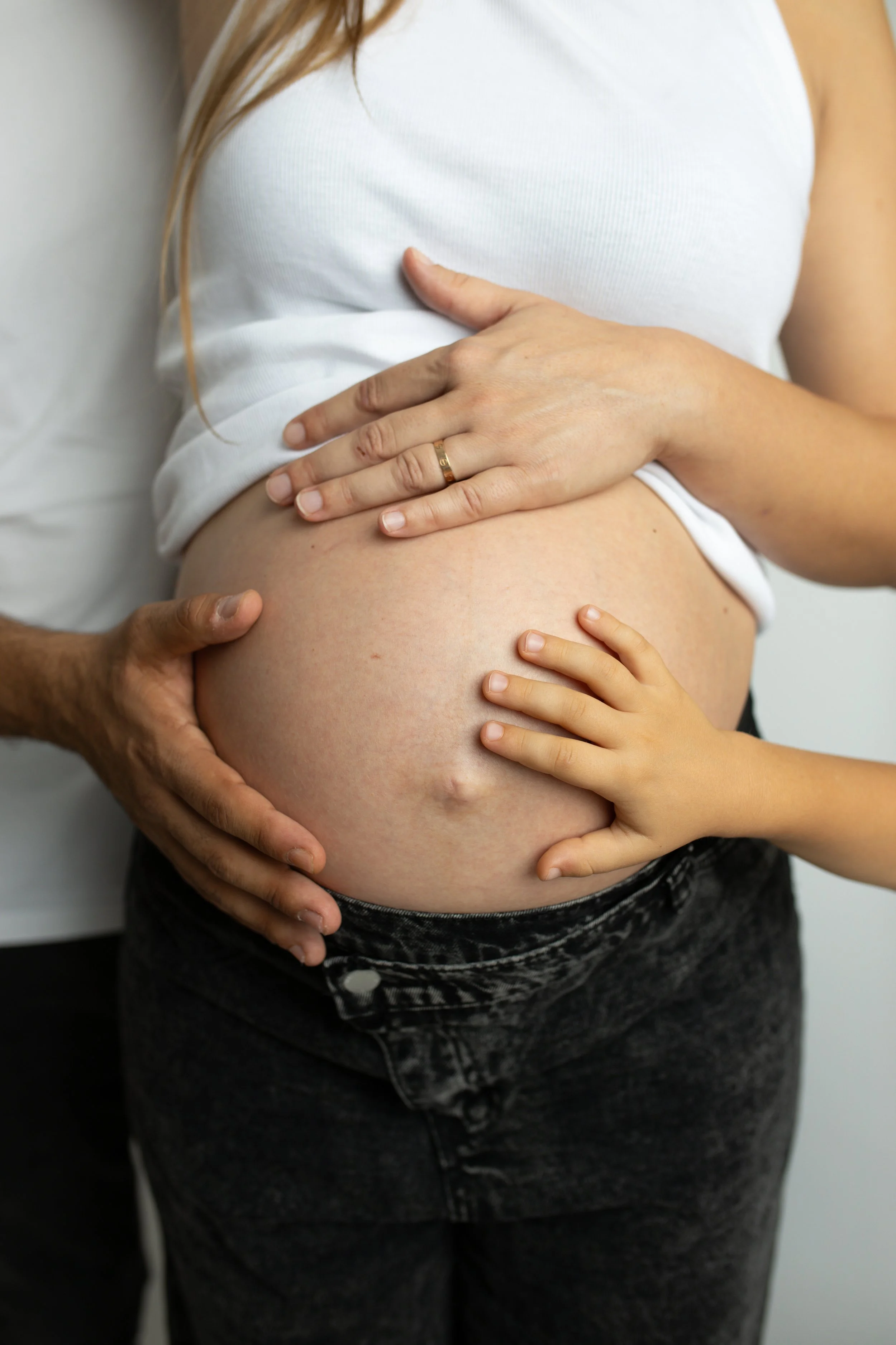 Une femme enceinte avec une main d'adulte et une main d'enfant posées sur son ventre, démontrant la grossesse.