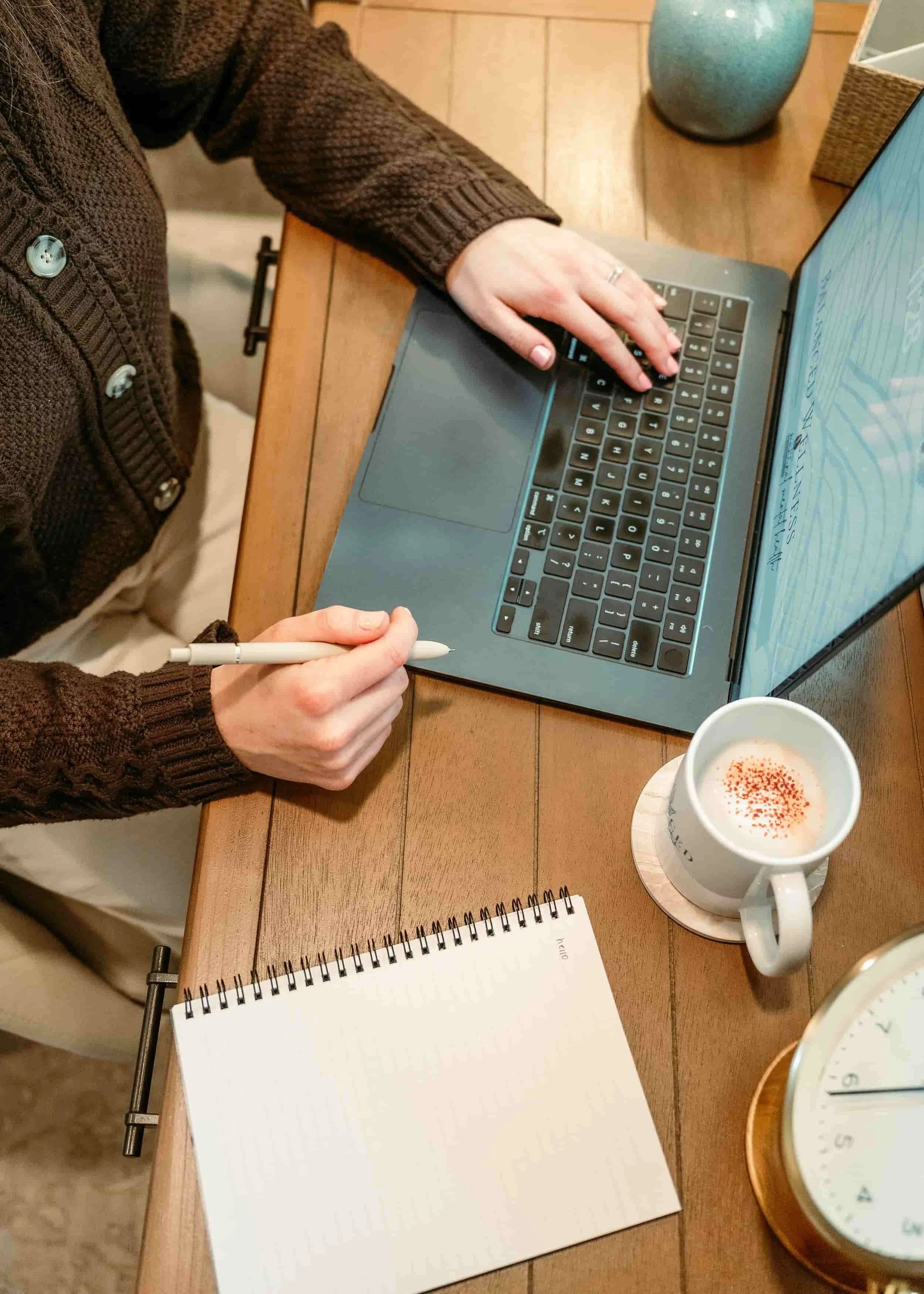 Woman sitting at table with her laptop coffee and notebook.