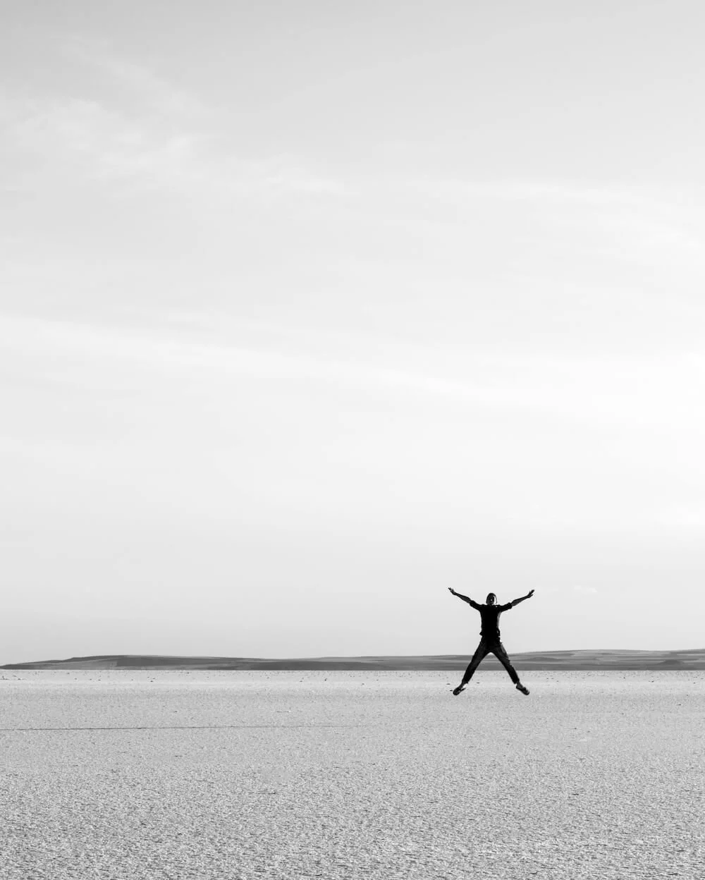 A young woman in a desert field jumping up in the air.