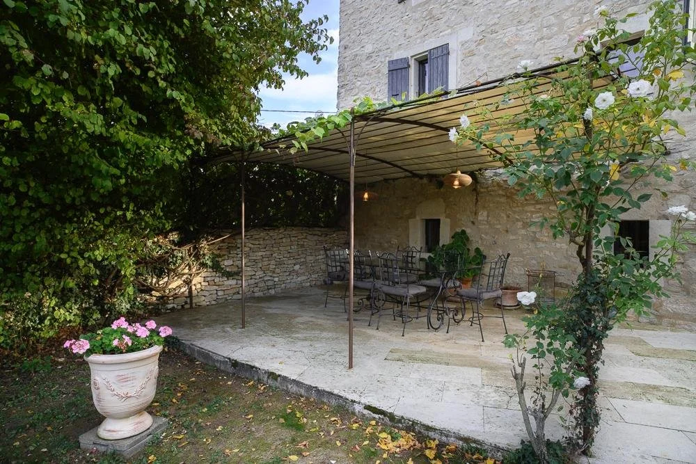 Outdoor patio area with a stone house, wrought iron furniture, a canopy, plants, and flowers.