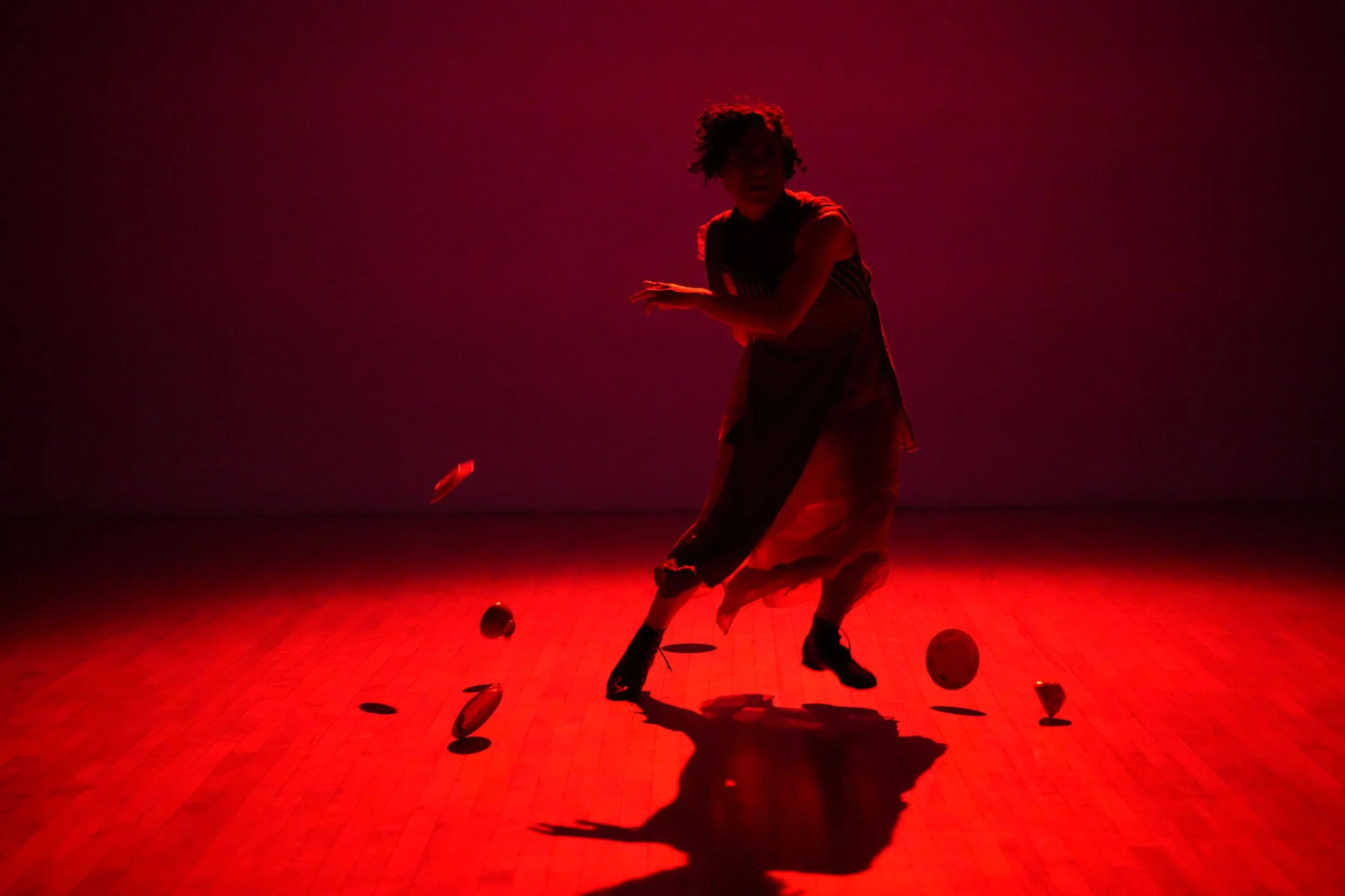 A person dancing in a dimly lit room with red lighting, surrounded by scattered objects on the floor.