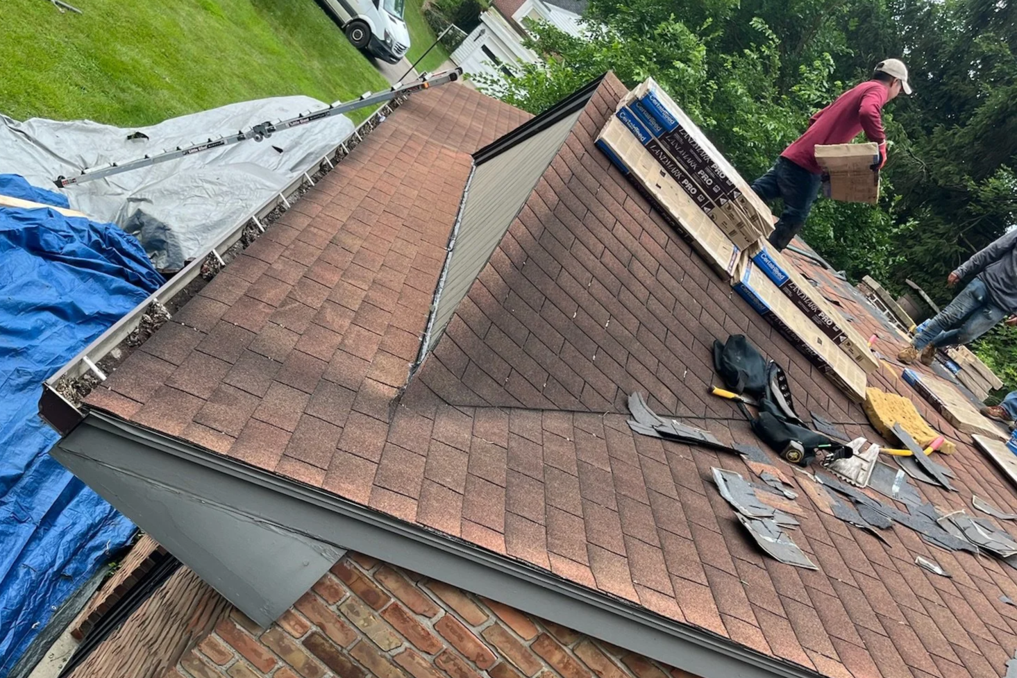 An old, worn roof that is being replaced. Some singles are lifted, and 3 men are working on re[placing it..