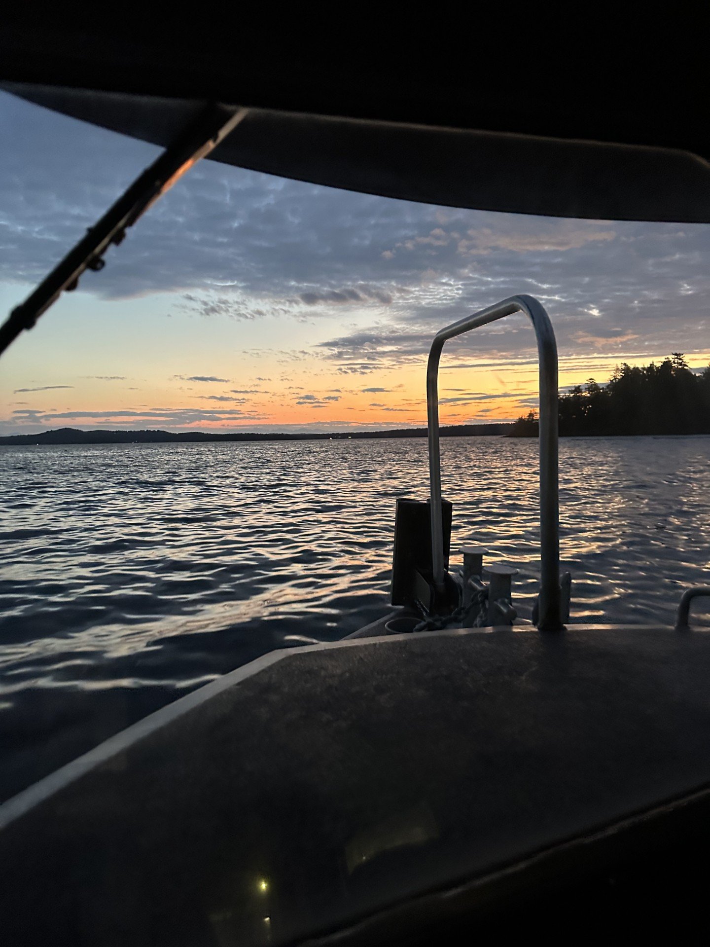 Sunset over a body of water viewed from the deck of a boat, with part of the boat's engine and railing visible in the foreground.