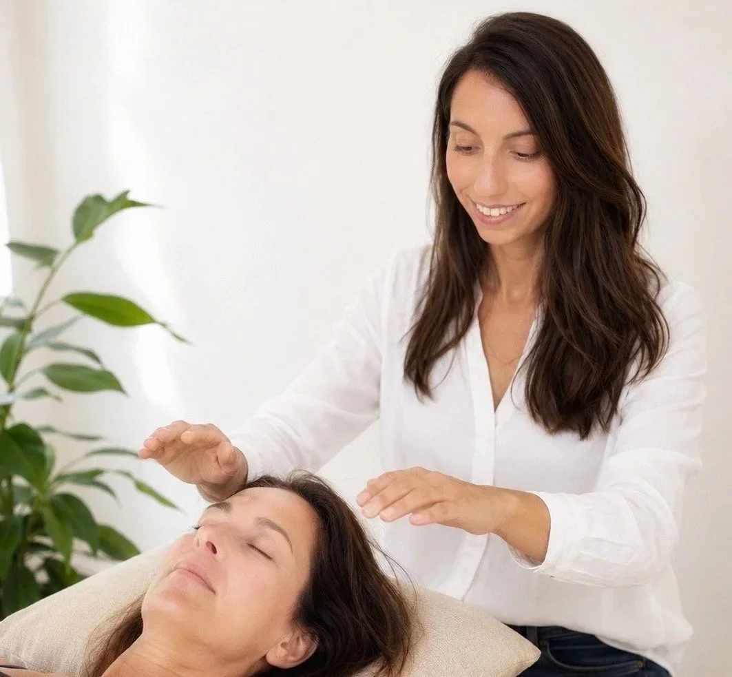A woman giving a healing or reiki treatment to another woman lying down with eyes closed.