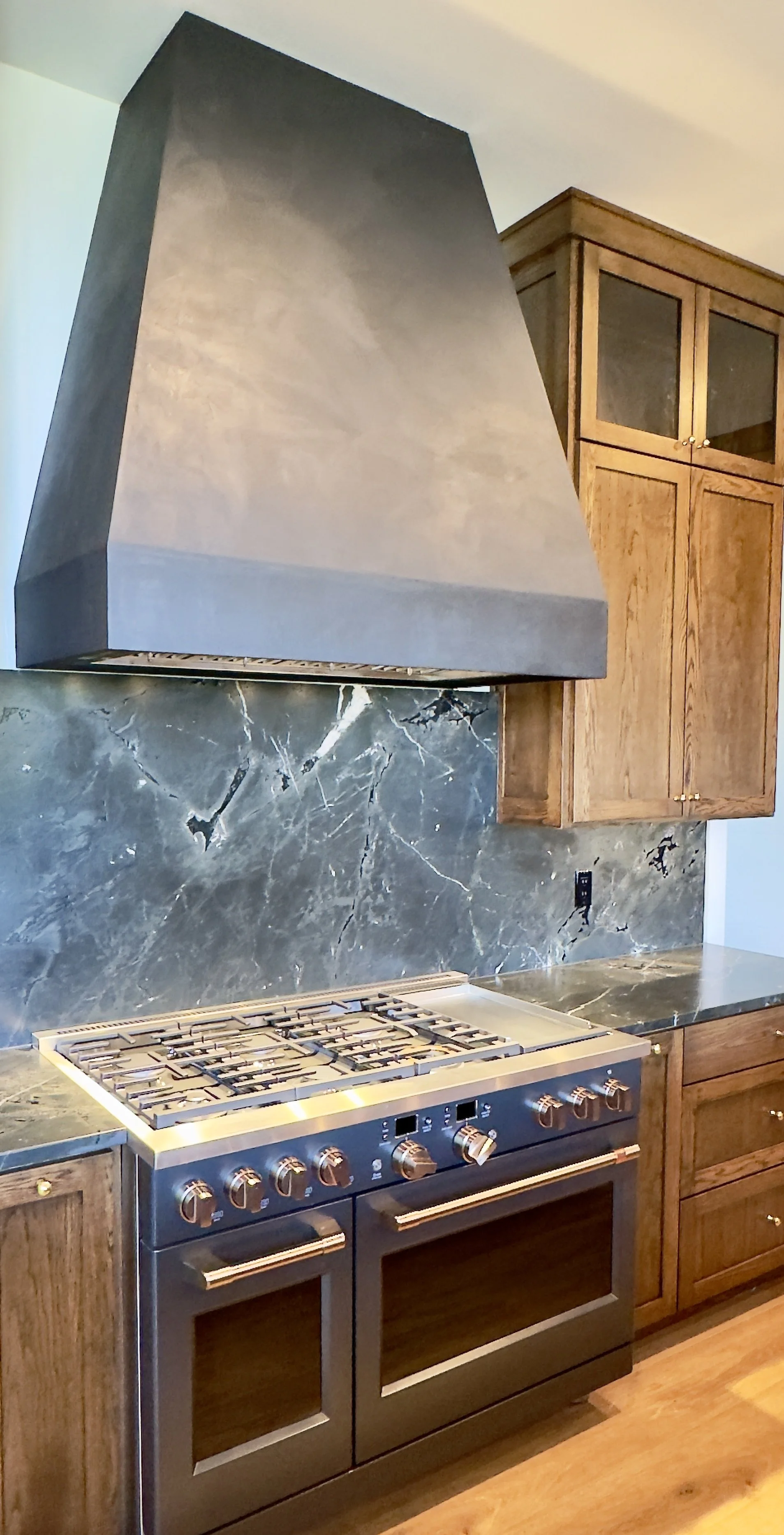 Kitchen stove with a black and gray marble backsplash and wooden cabinets.